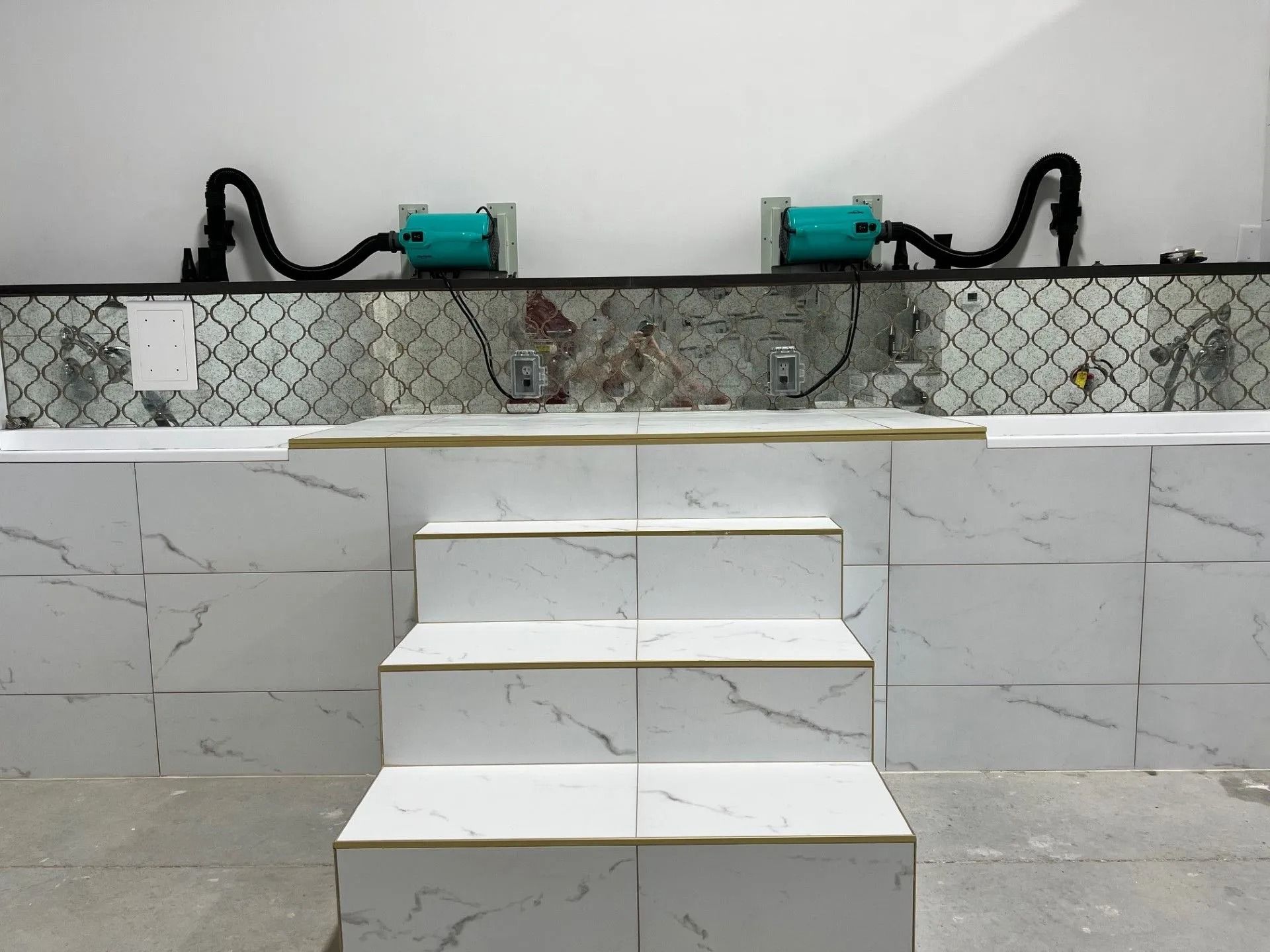 A partially tiled indoor pool under construction with steps, equipment on the back wall.