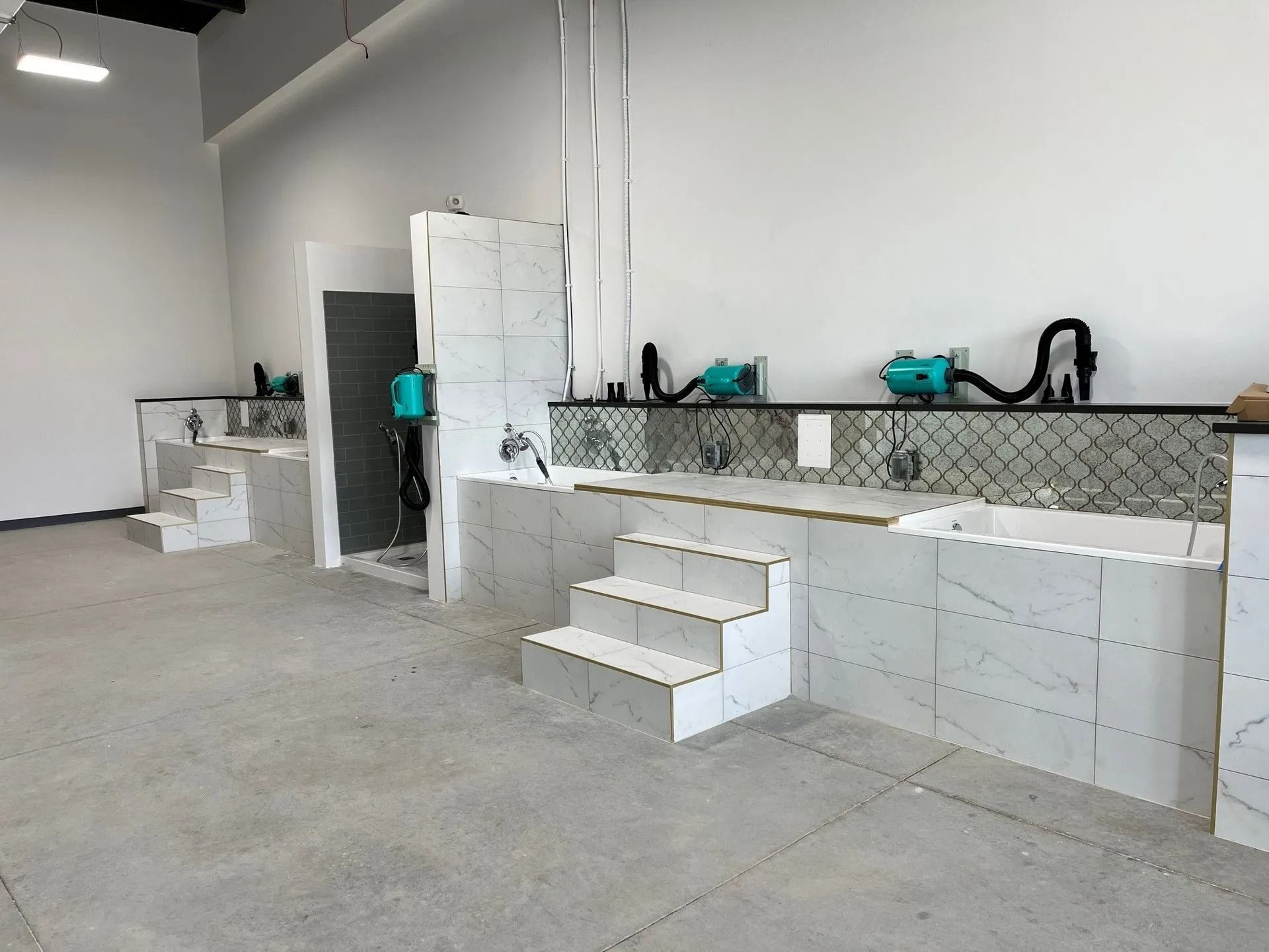 Interior of a dog grooming salon with multiple washing stations under construction. White tile and unfinished walls.