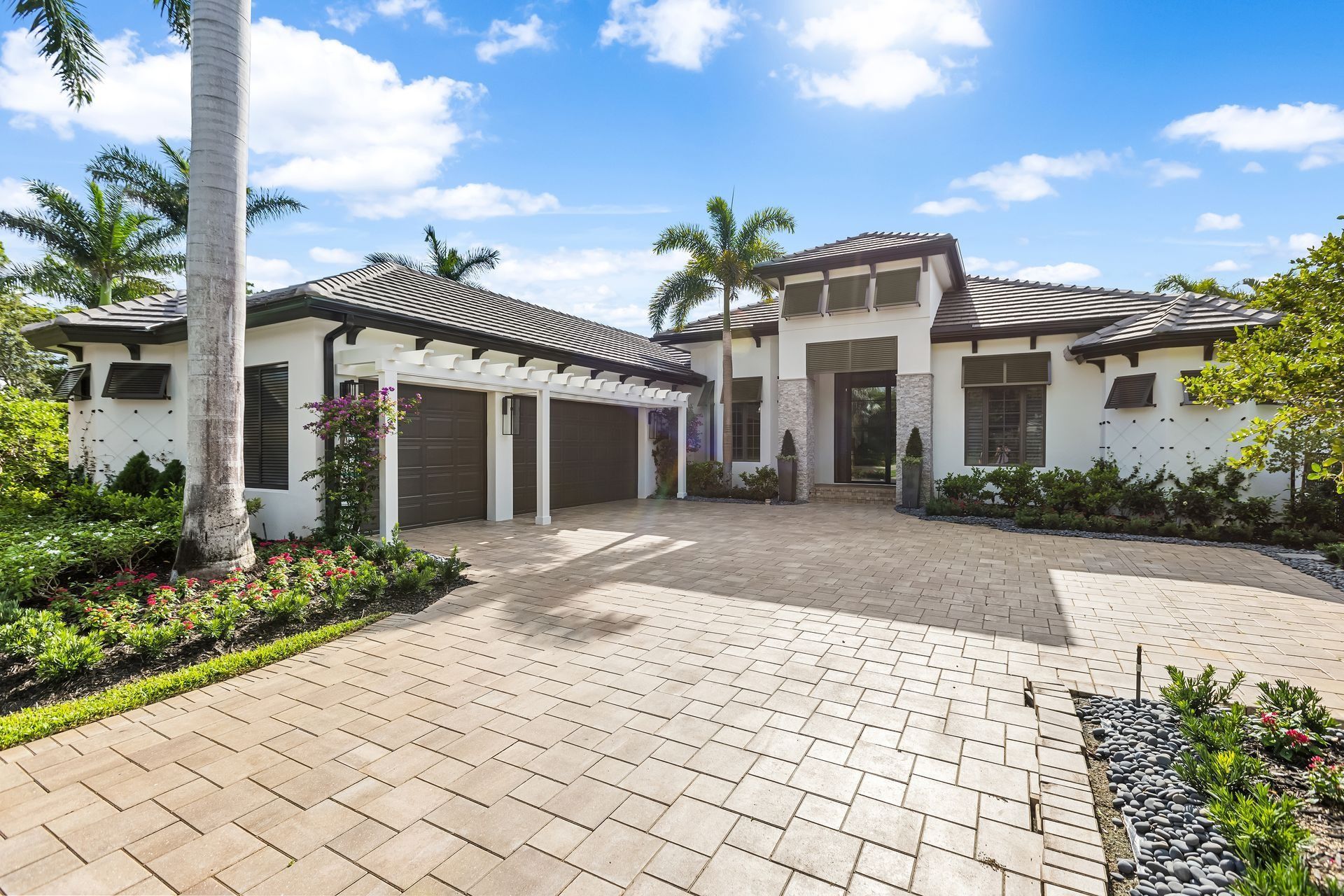 Luxury home with a brick driveway, attached garage, and palm trees under a bright blue sky.