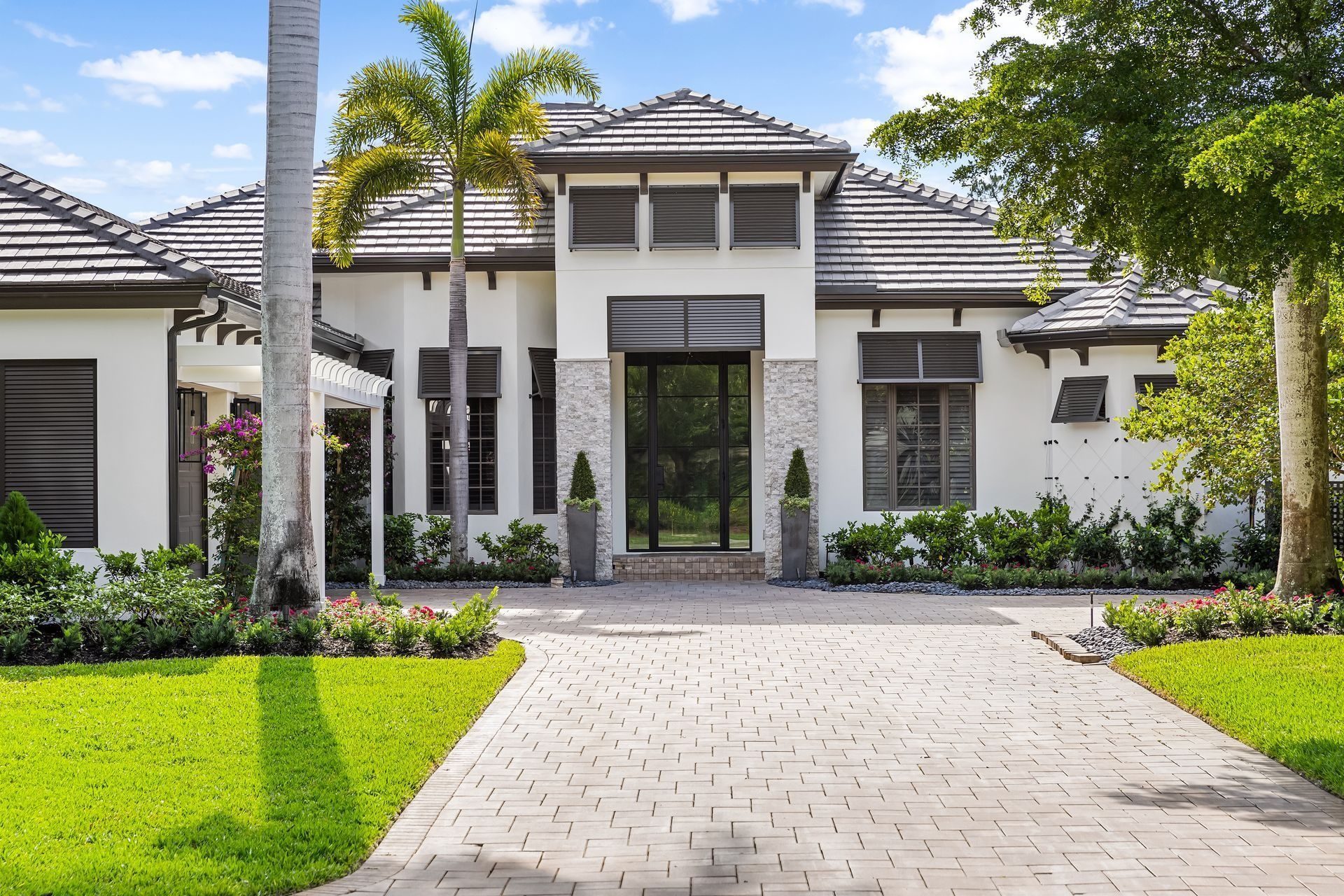 Elegant white home with stone driveway, lush green lawn, and palm trees.