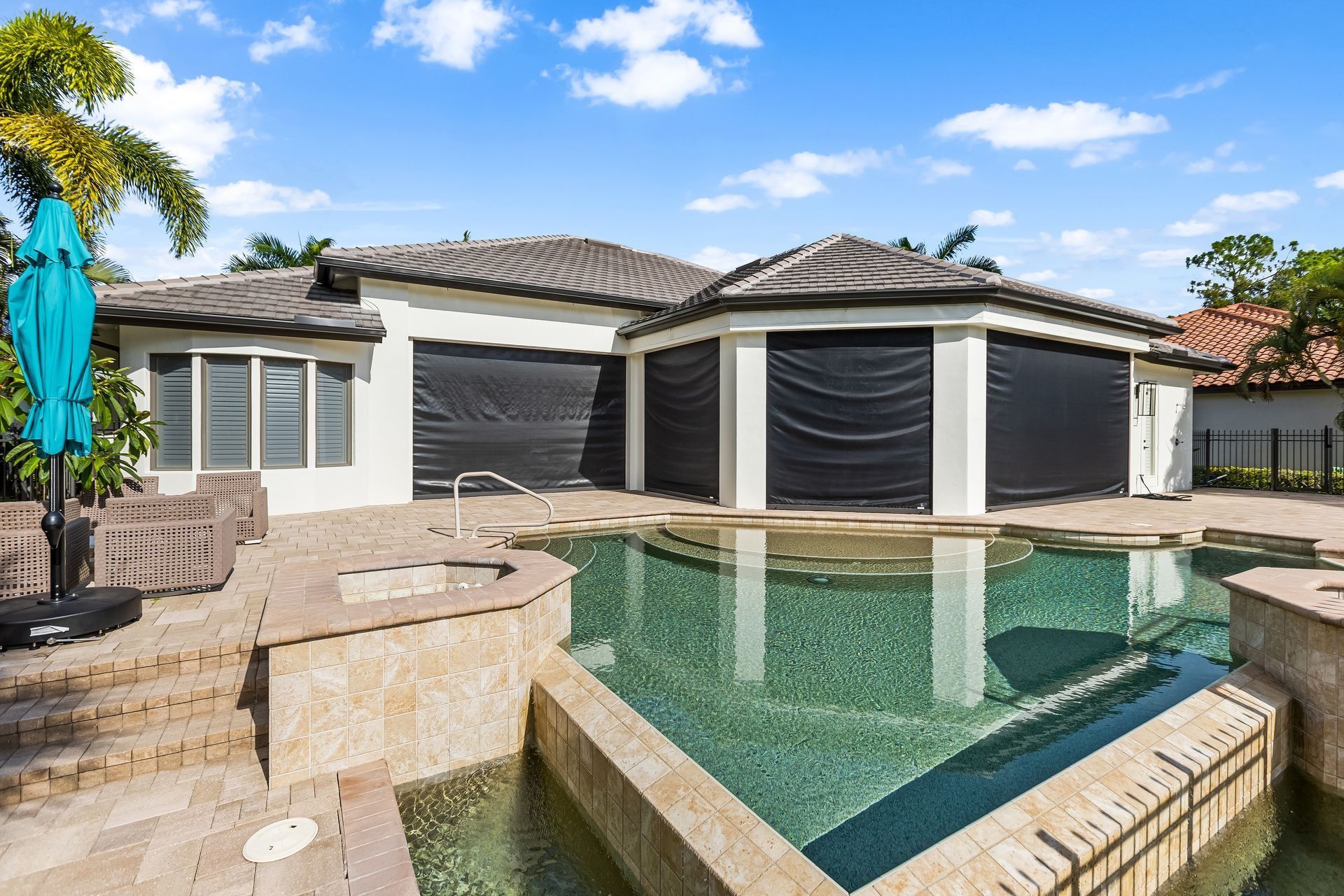 A house with a pool and dark window coverings under a partly cloudy sky.