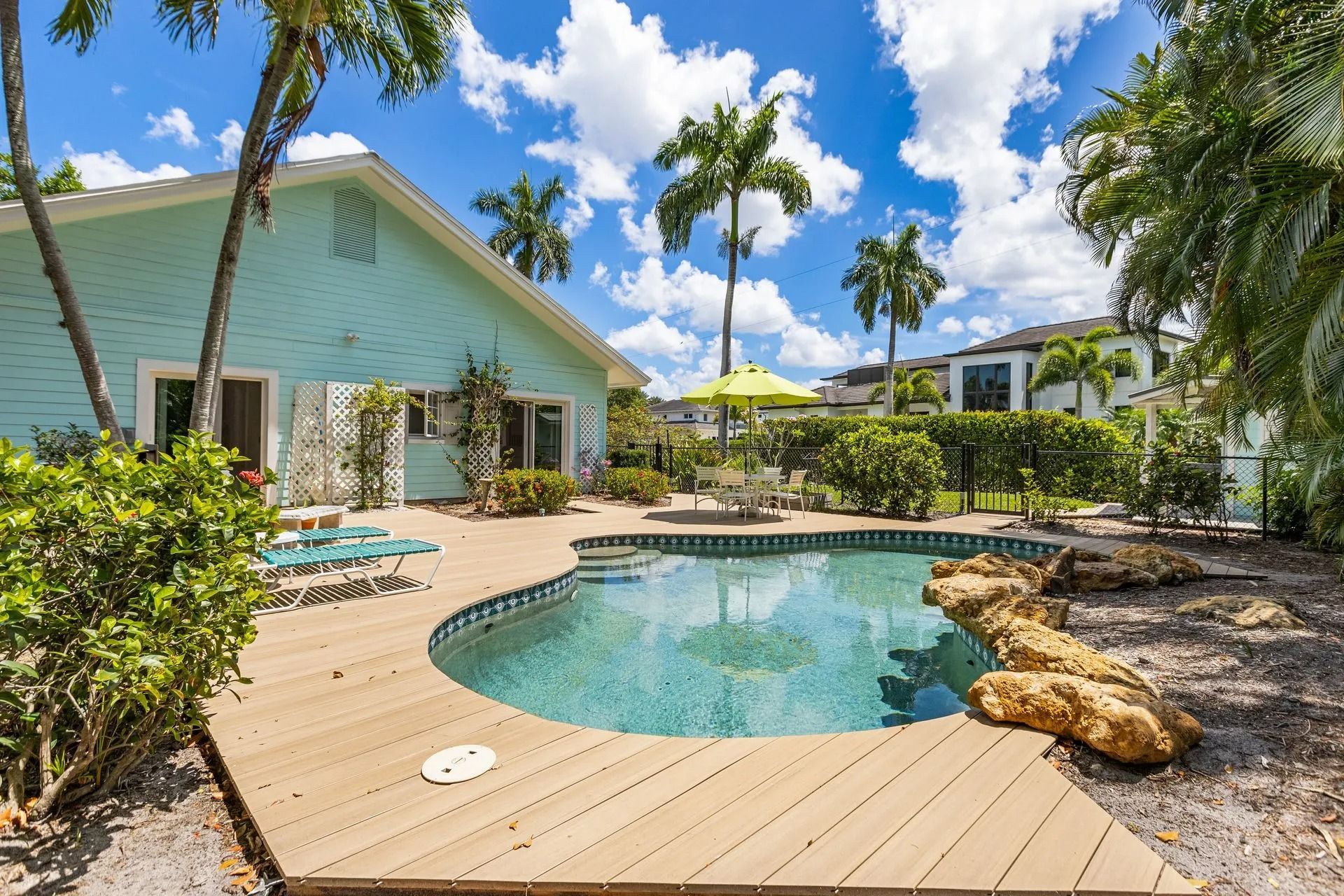 Backyard with turquoise house, pool, palm trees, and sunny blue sky.