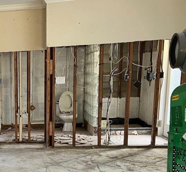 Bathroom undergoing renovation, walls open to studs, toilet visible, electrical and plumbing exposed.