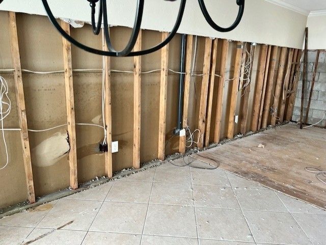 Interior wall gutted to studs, exposed electrical wiring and plumbing.  Floor tiled, some wood flooring remains.