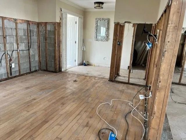 Room under renovation; walls gutted, wooden floor exposed. Electrical wires visible.