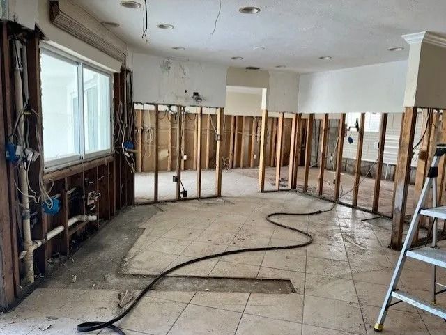 Interior gutted room with exposed studs, wiring, and damaged tile floor. A ladder leans against a wall.