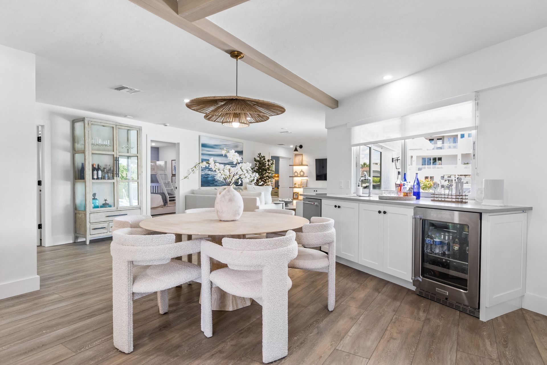 Dining area with round table, white chairs, and a built-in wet bar. Light wood floors and neutral tones.