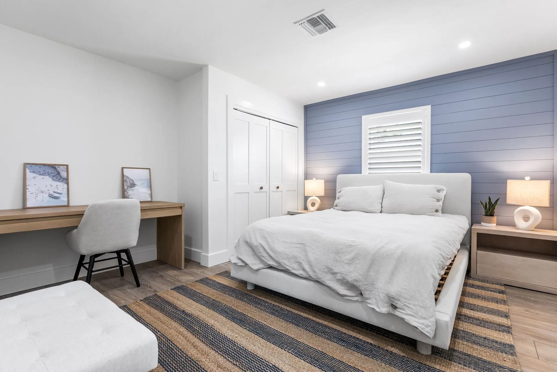Bedroom with bed, desk, blue accent wall, white closet doors, wooden floors.
