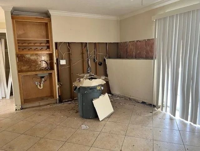 Kitchen undergoing renovation, cabinetry and drywall removed, trash can present, tiled floor.