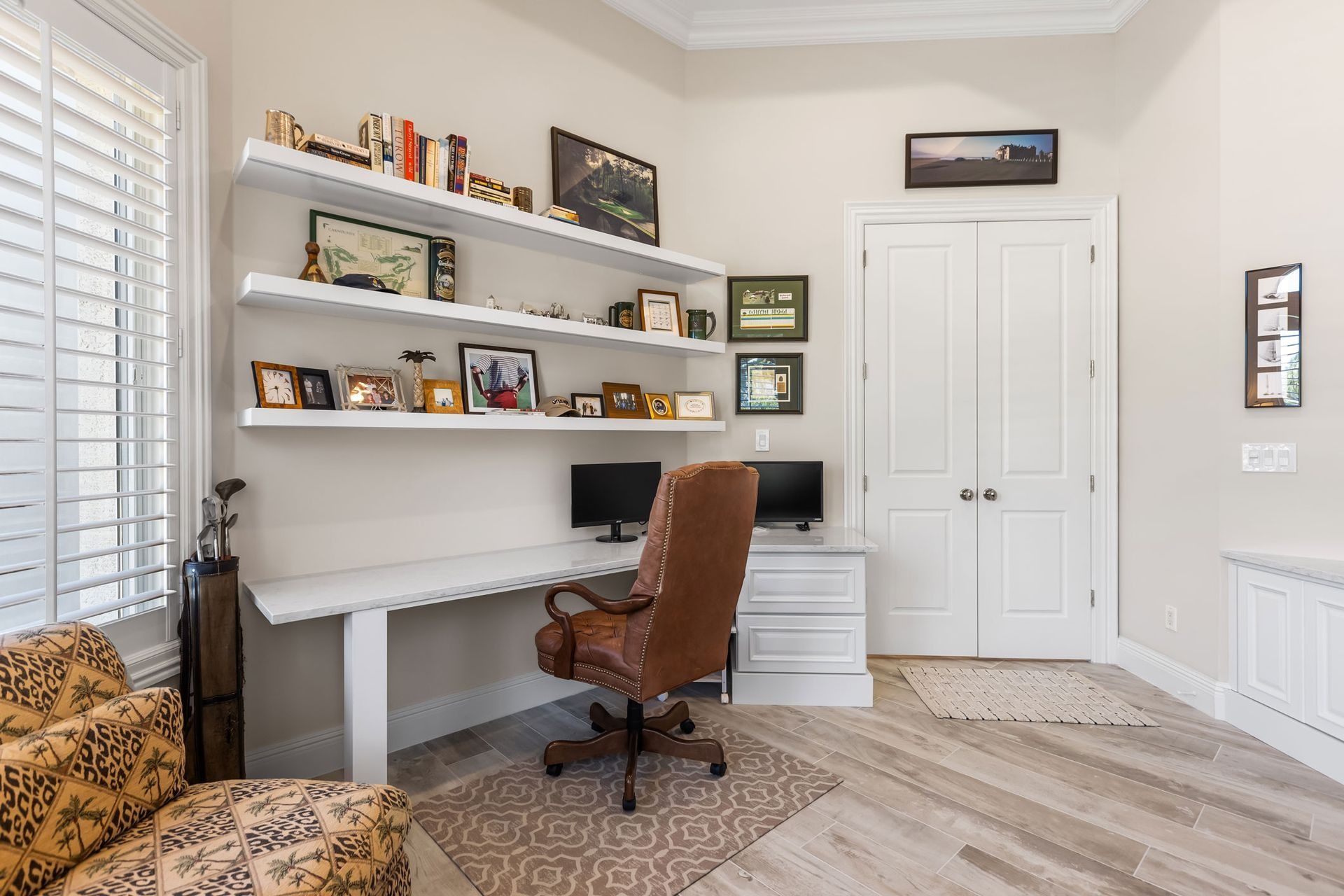 Home office with white desk, shelving, brown leather chair, and wooden floor.