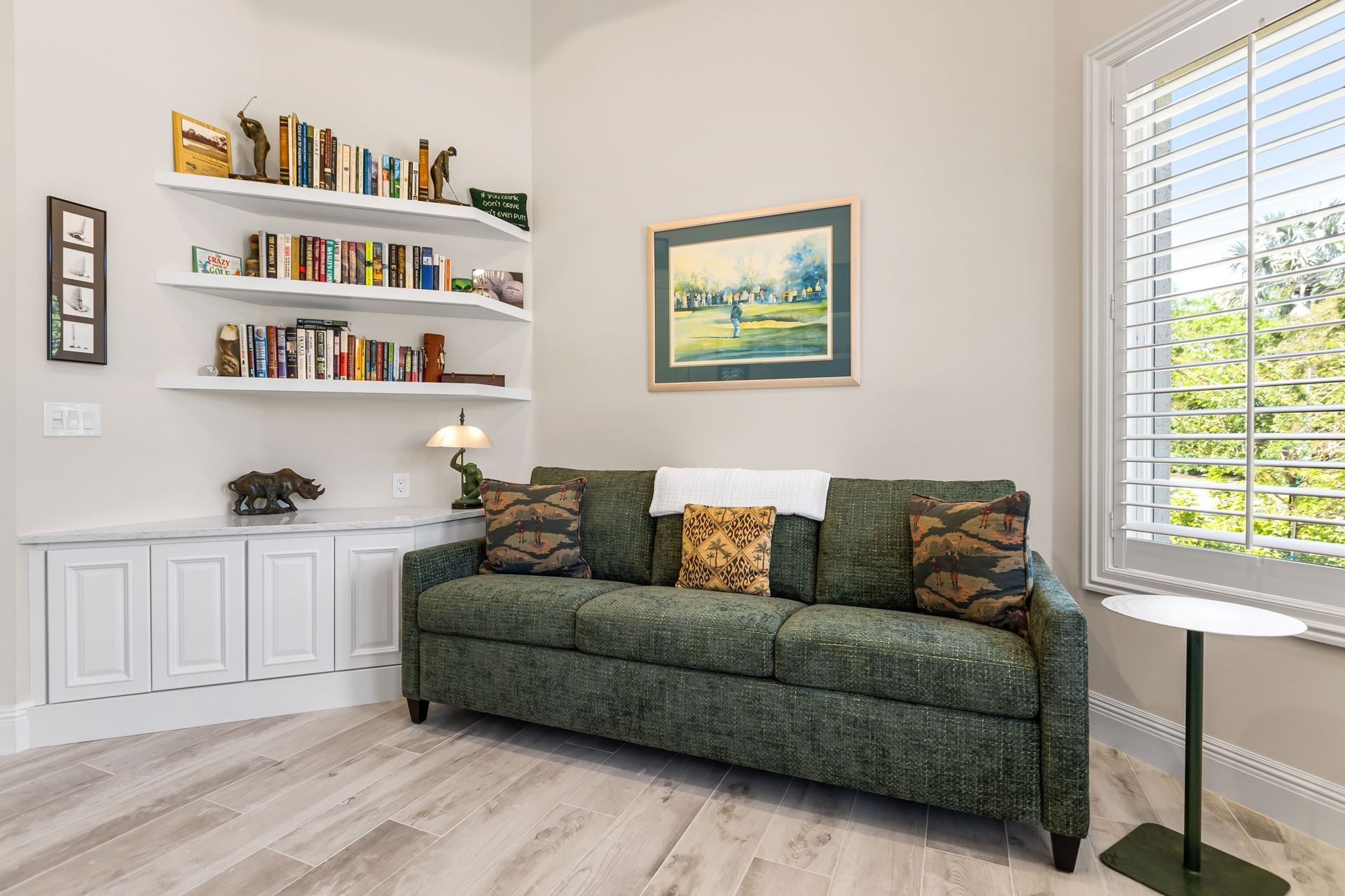 Living room with green sofa, built-in shelves of books, white cabinets, and a window with blinds.