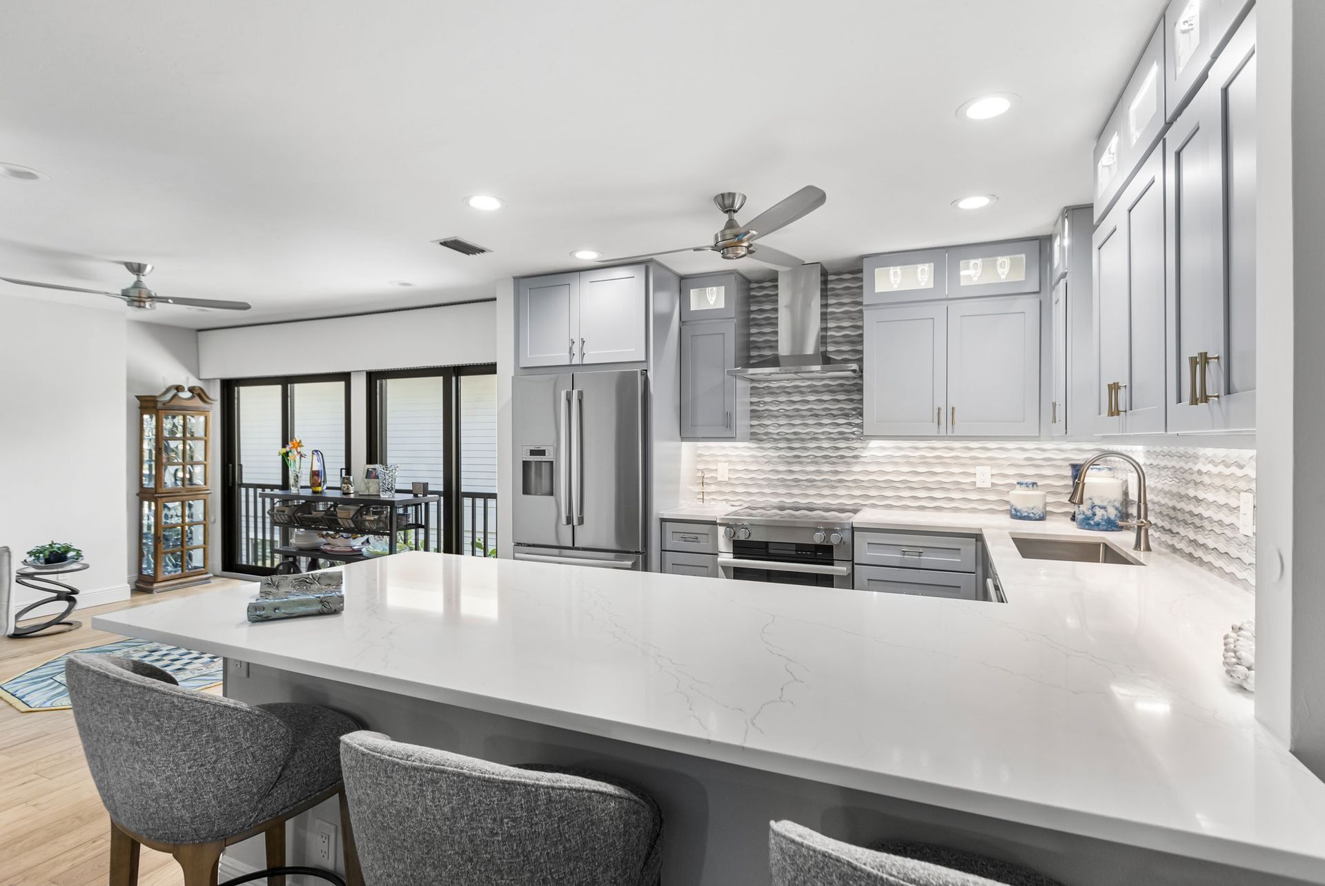 Modern kitchen with gray cabinets, white countertops, and bar stools.