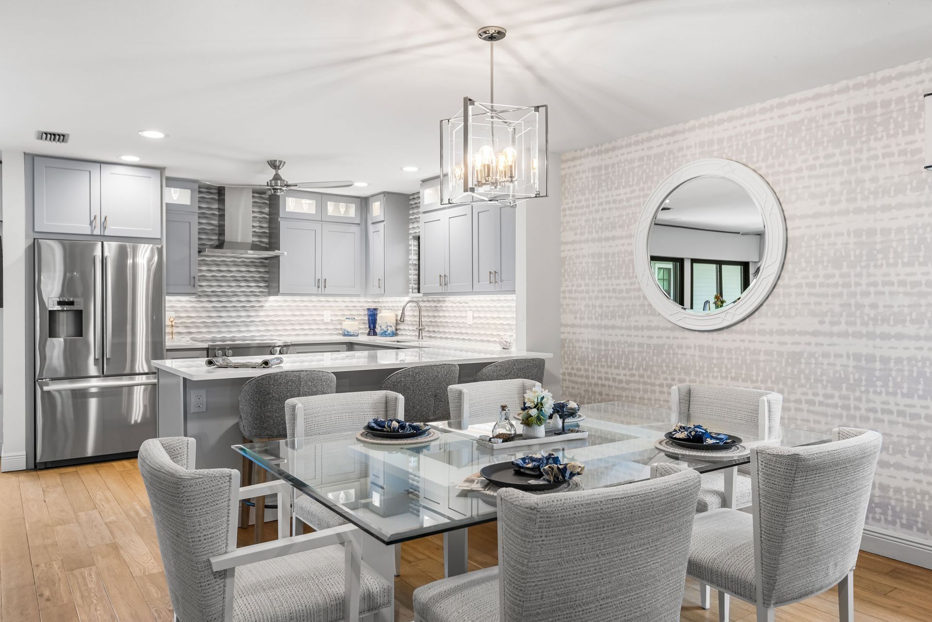 Modern kitchen and dining room with gray cabinets, glass table, and light-colored chairs.