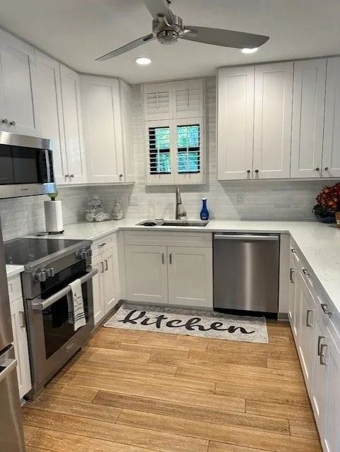 White kitchen with light wood floor. Stainless steel appliances, white cabinets, and a window above the sink.