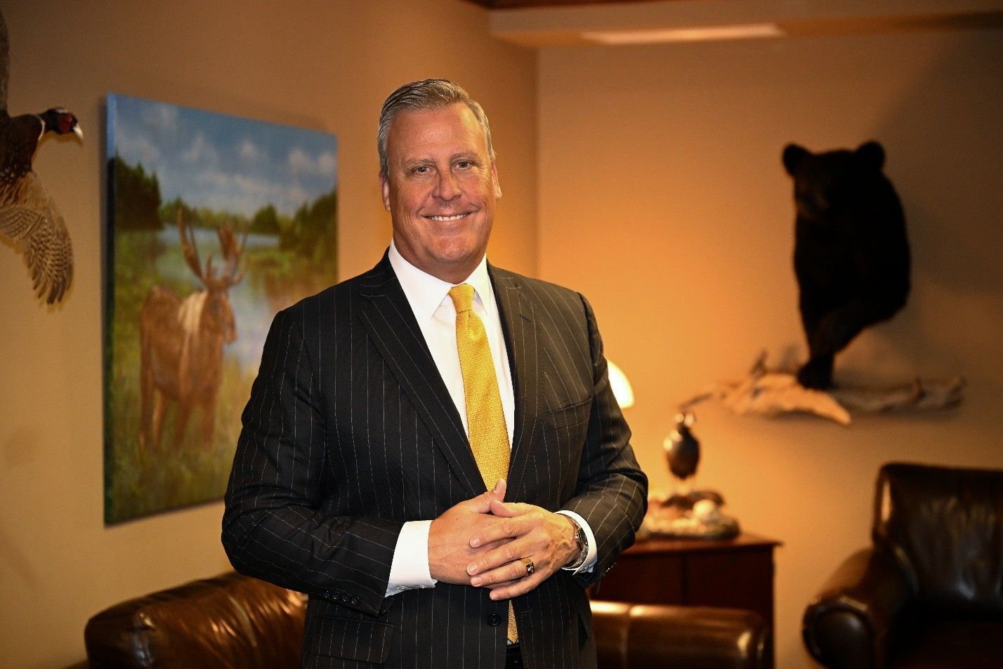 A person in a suit and glasses sits at a desk, reviewing open books in a professional office.