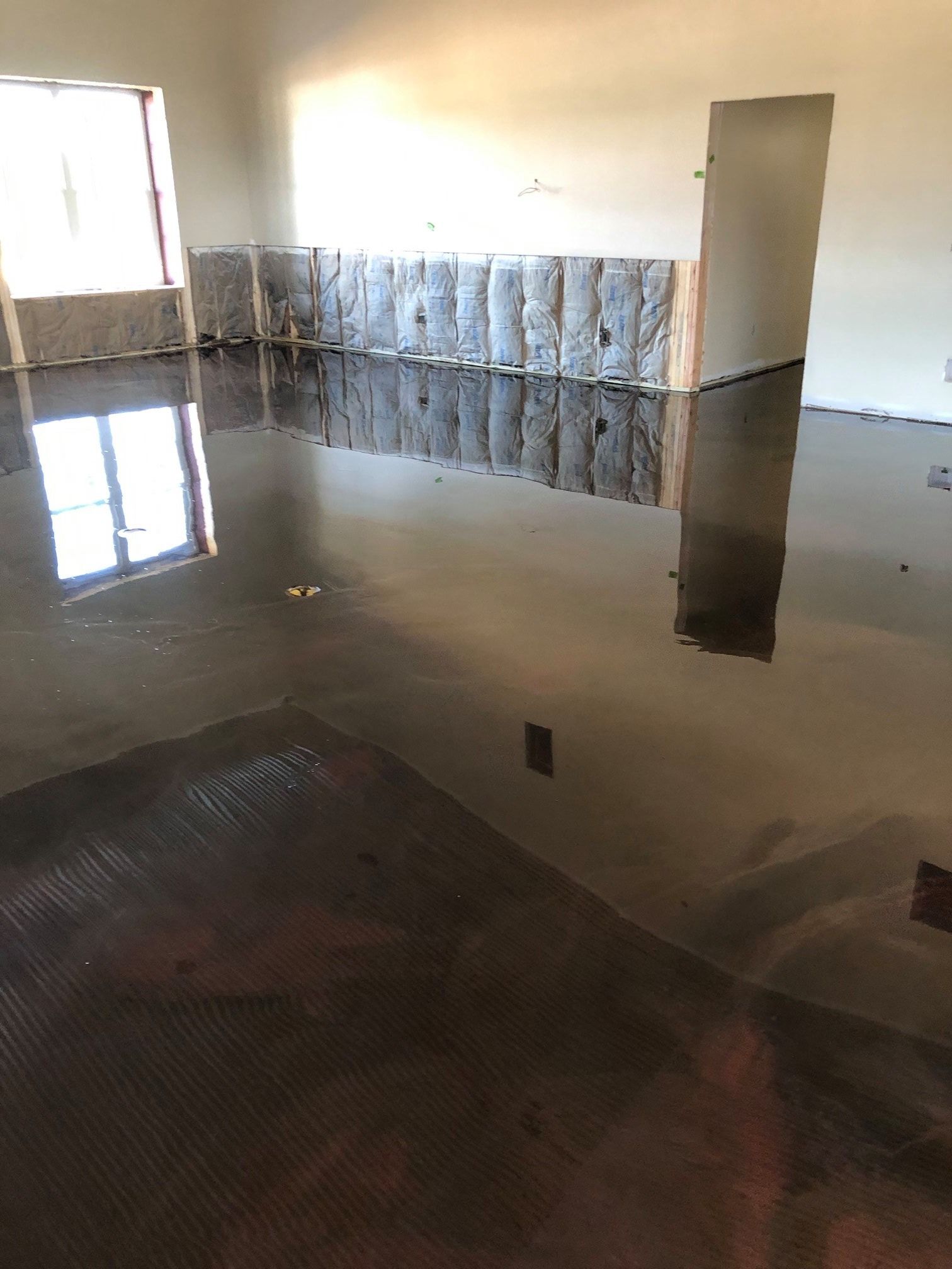 A room with a flooded floor and a reflection of a window in the floor.