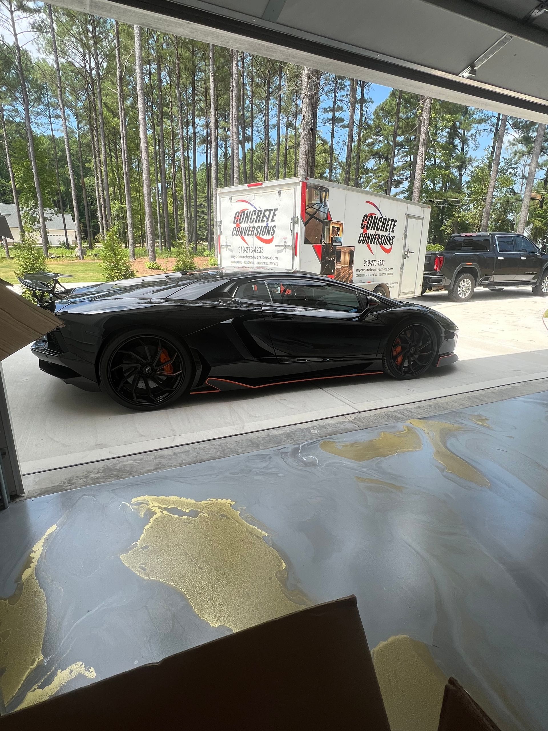A black lamborghini aventador is parked in a garage next to a moving truck.