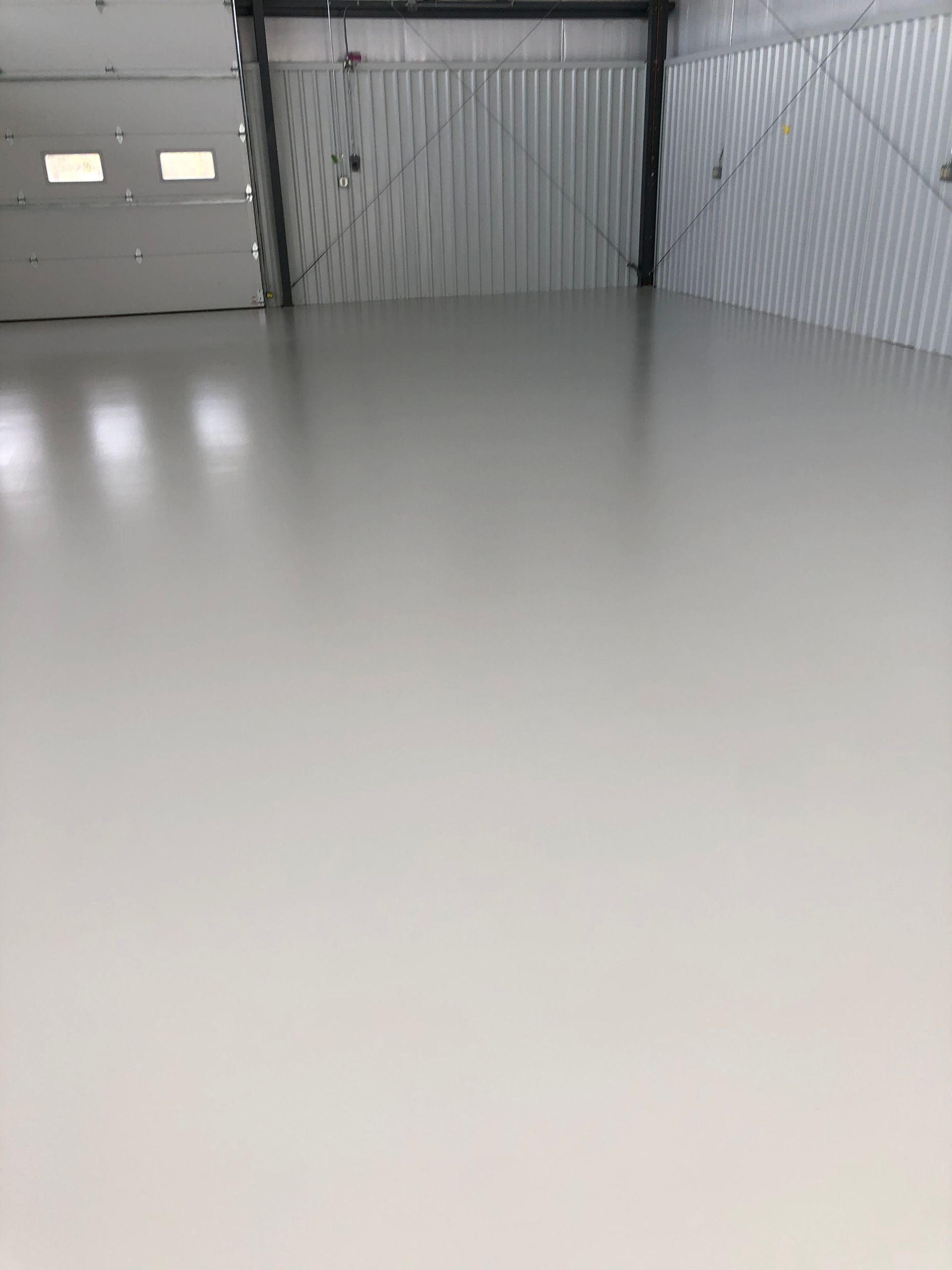 A large empty room with a white floor and a garage door.