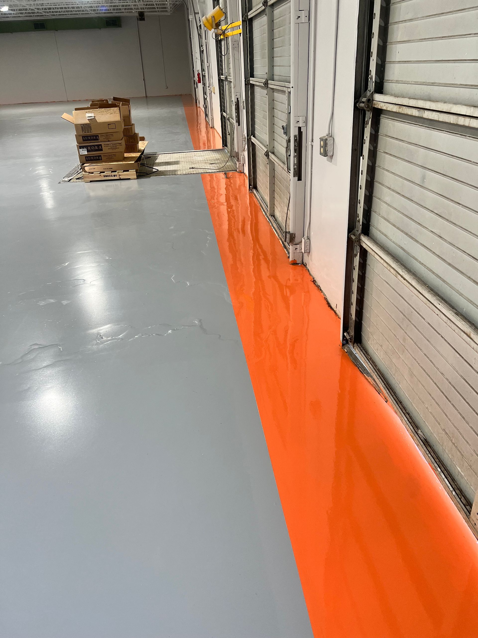 A warehouse with a gray and orange floor and a row of garage doors.