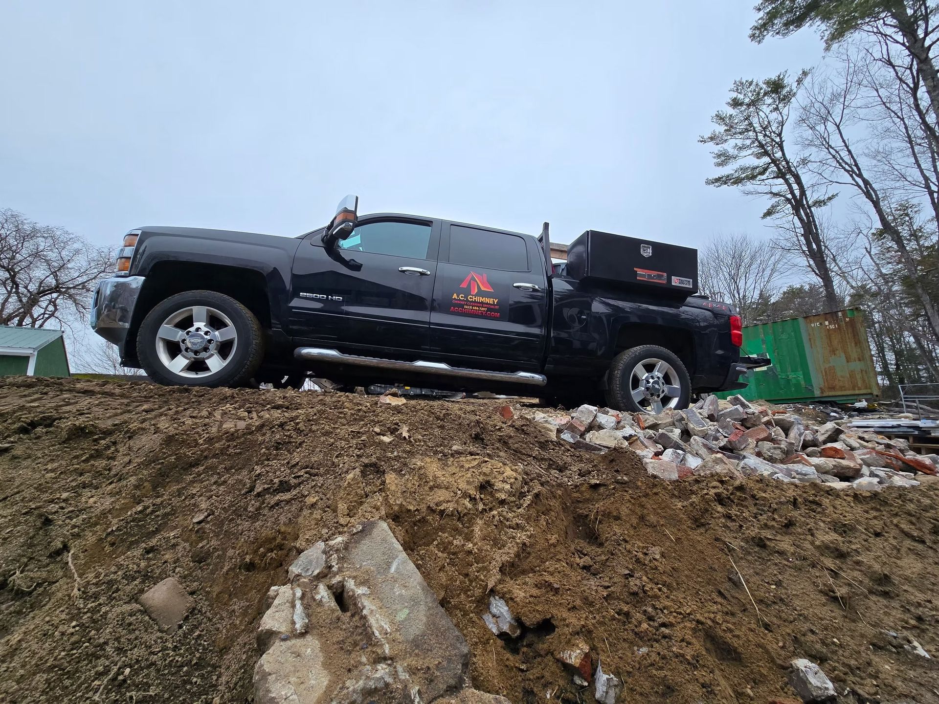 Black pickup truck parked on a dirt mound at a construction site under a cloudy sky