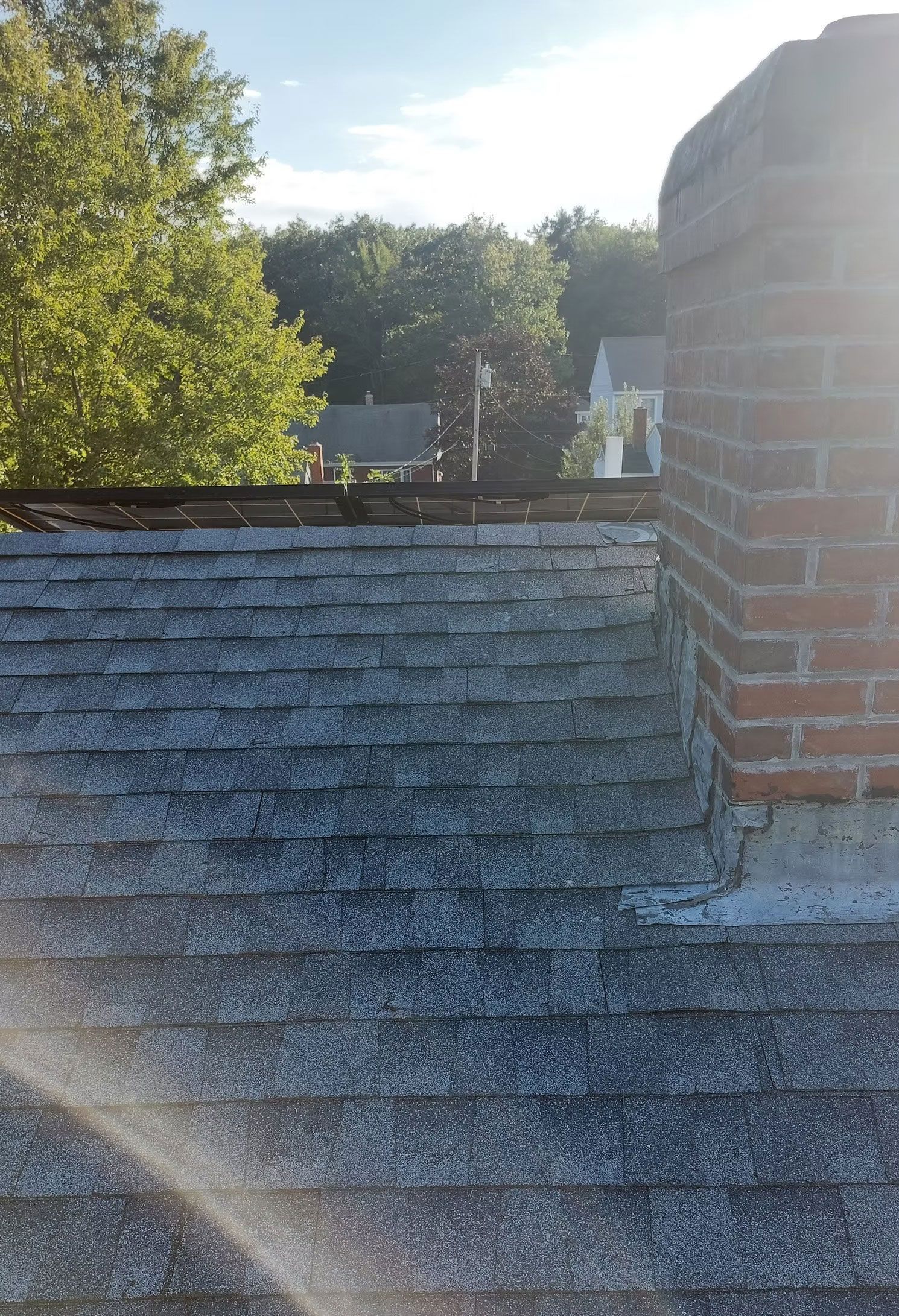 Sunlit rooftop with a brick chimney and trees in the background
