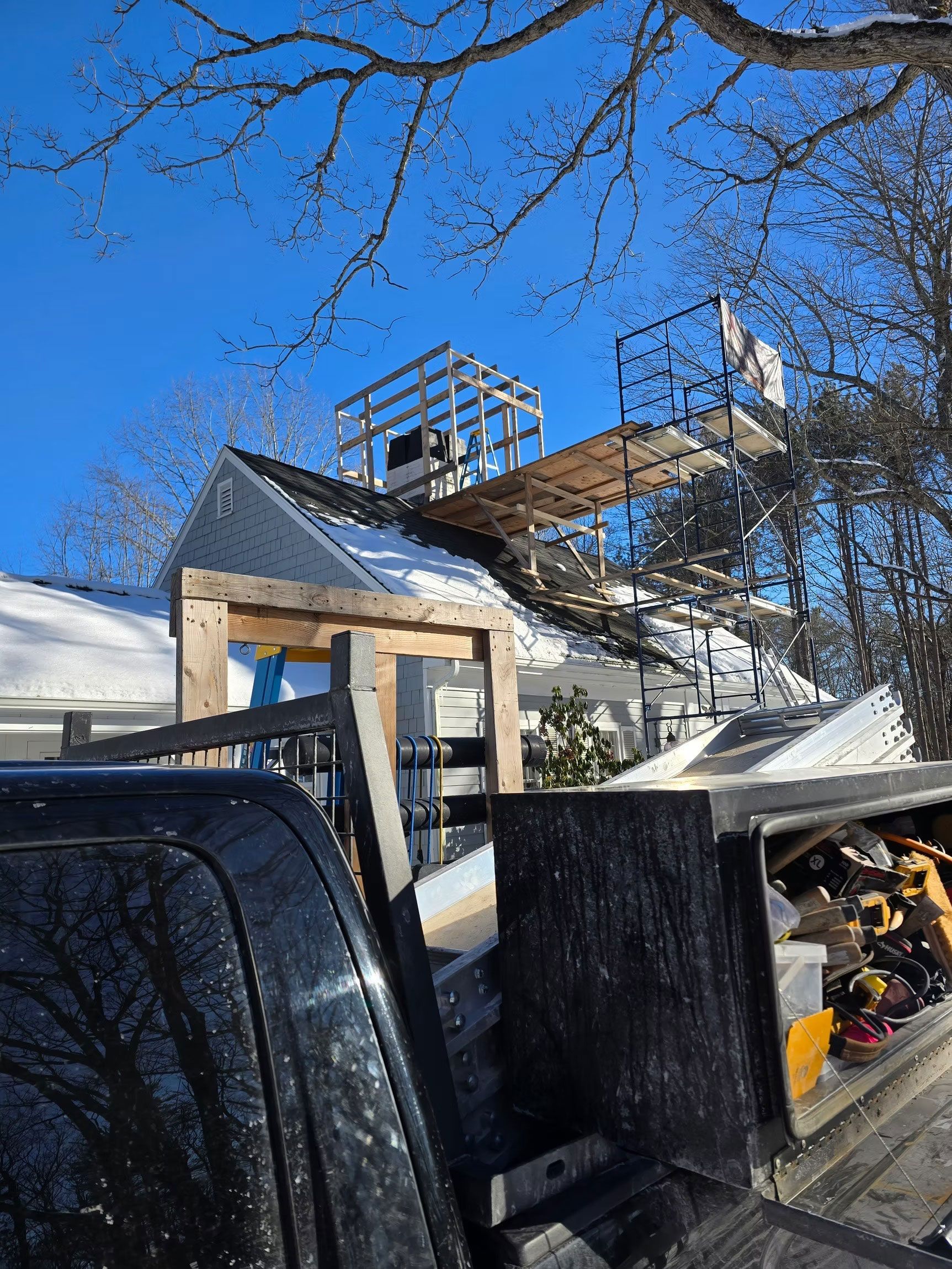 Snowy rooftop construction site with exposed framing and ladders under a clear blue sky