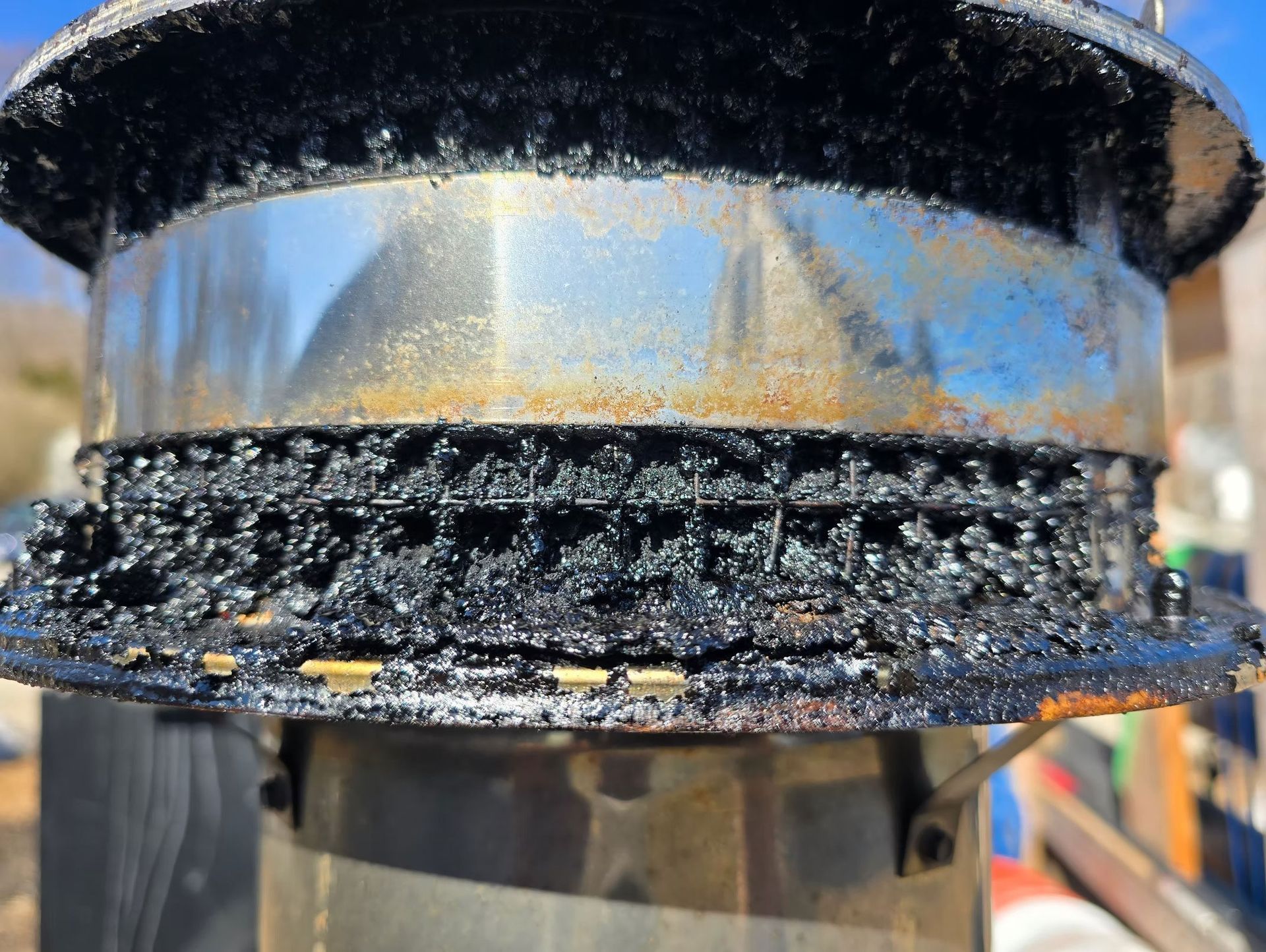 Close-up of a metal pipe flange with black residue and rust stains outdoors