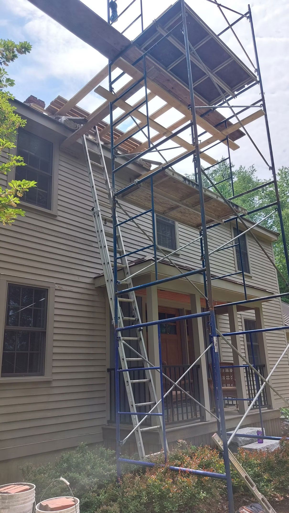 House with tall metal scaffolding and roof work in progress, viewed from the front yard