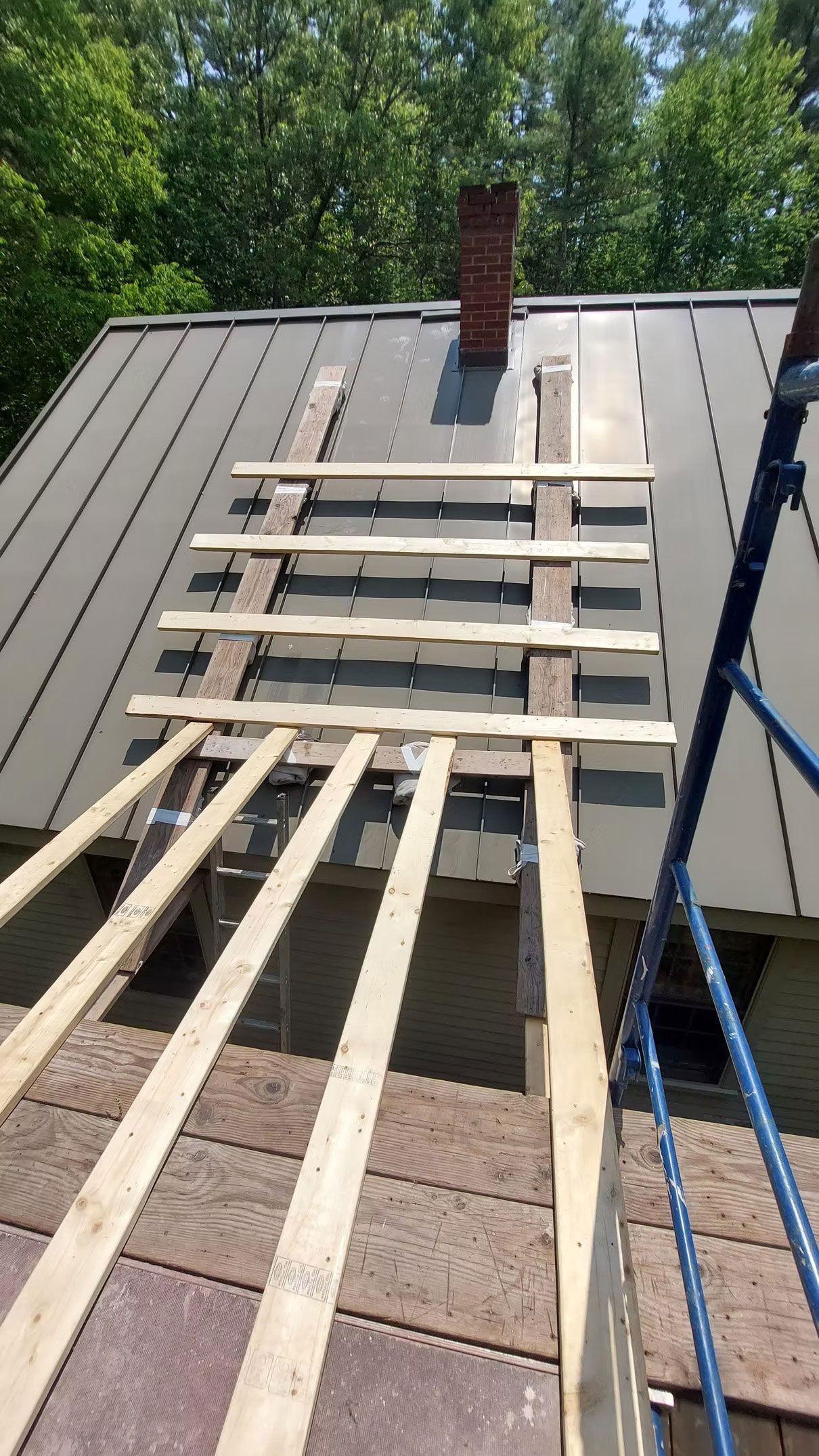 Wooden roof scaffolding and planks leading up to a chimney on a sloped metal roof