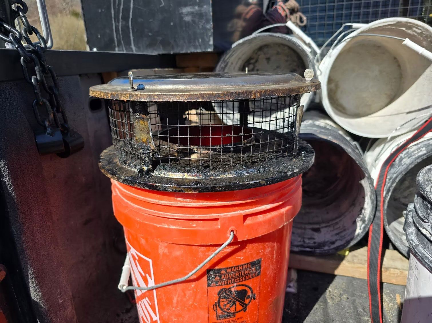 Orange bucket holding a black wire cage and filter parts beside stacked white buckets outdoors