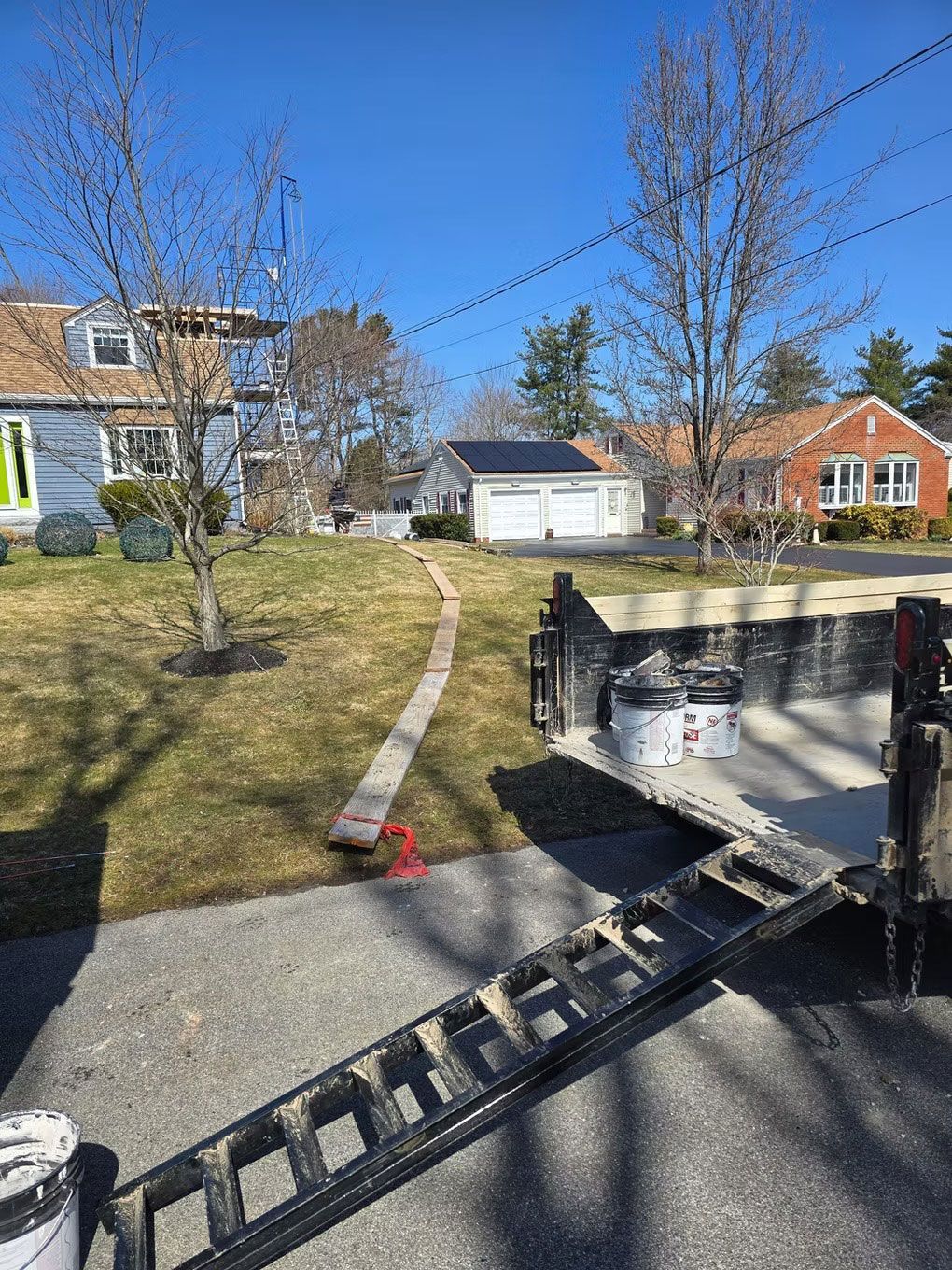 Black trailer ramp leading to a driveway in a suburban neighborhood on a sunny day
