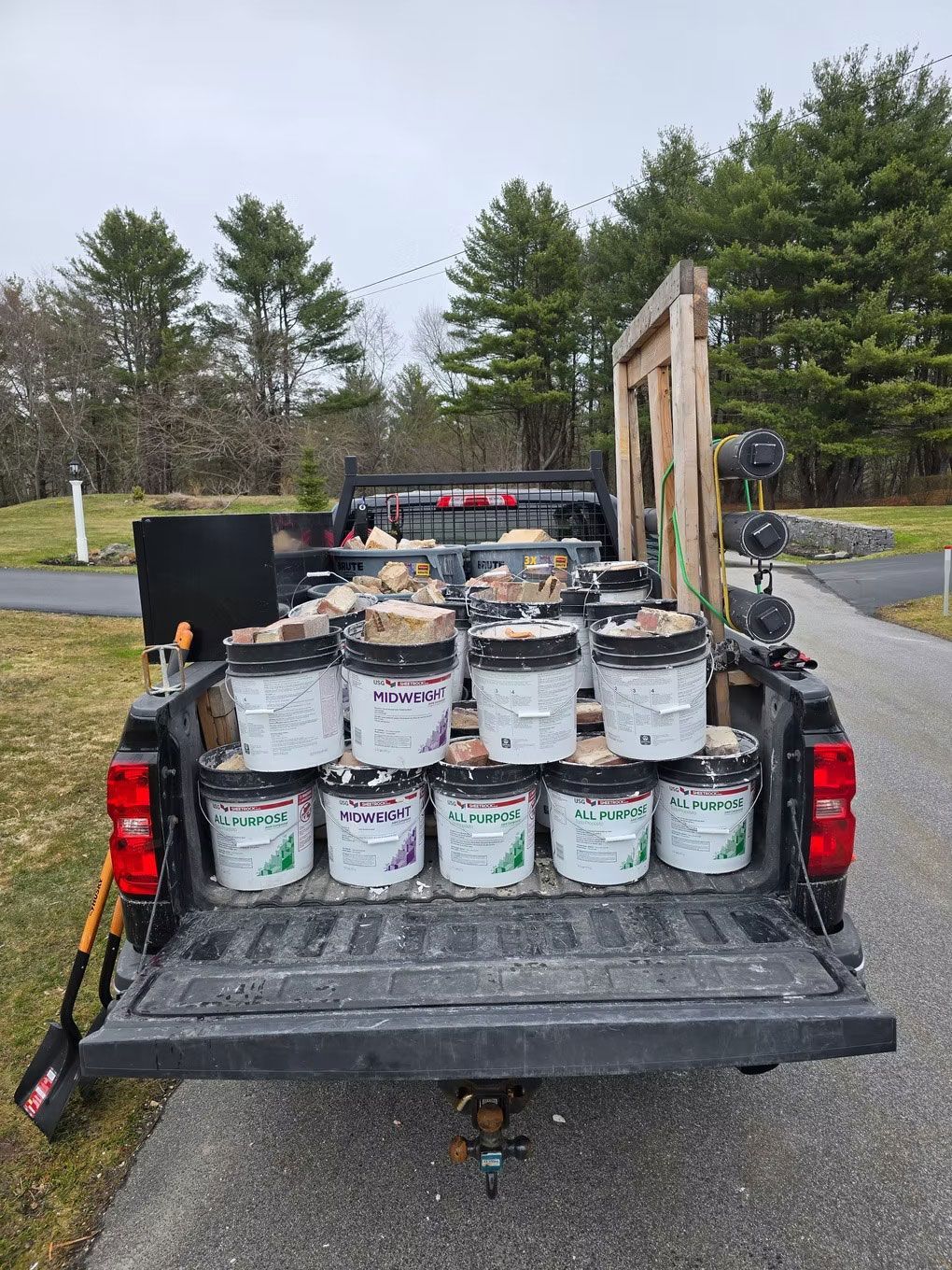 Pickup truck bed loaded with paint buckets and tools at a roadside worksite