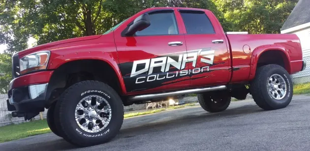 Red pickup truck with DANK Collision logo parked outdoors on a sloped road