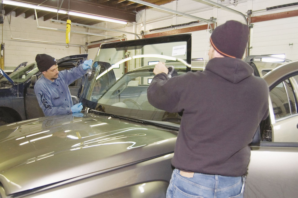 Two workers inspecting a car windshield in an auto repair shop