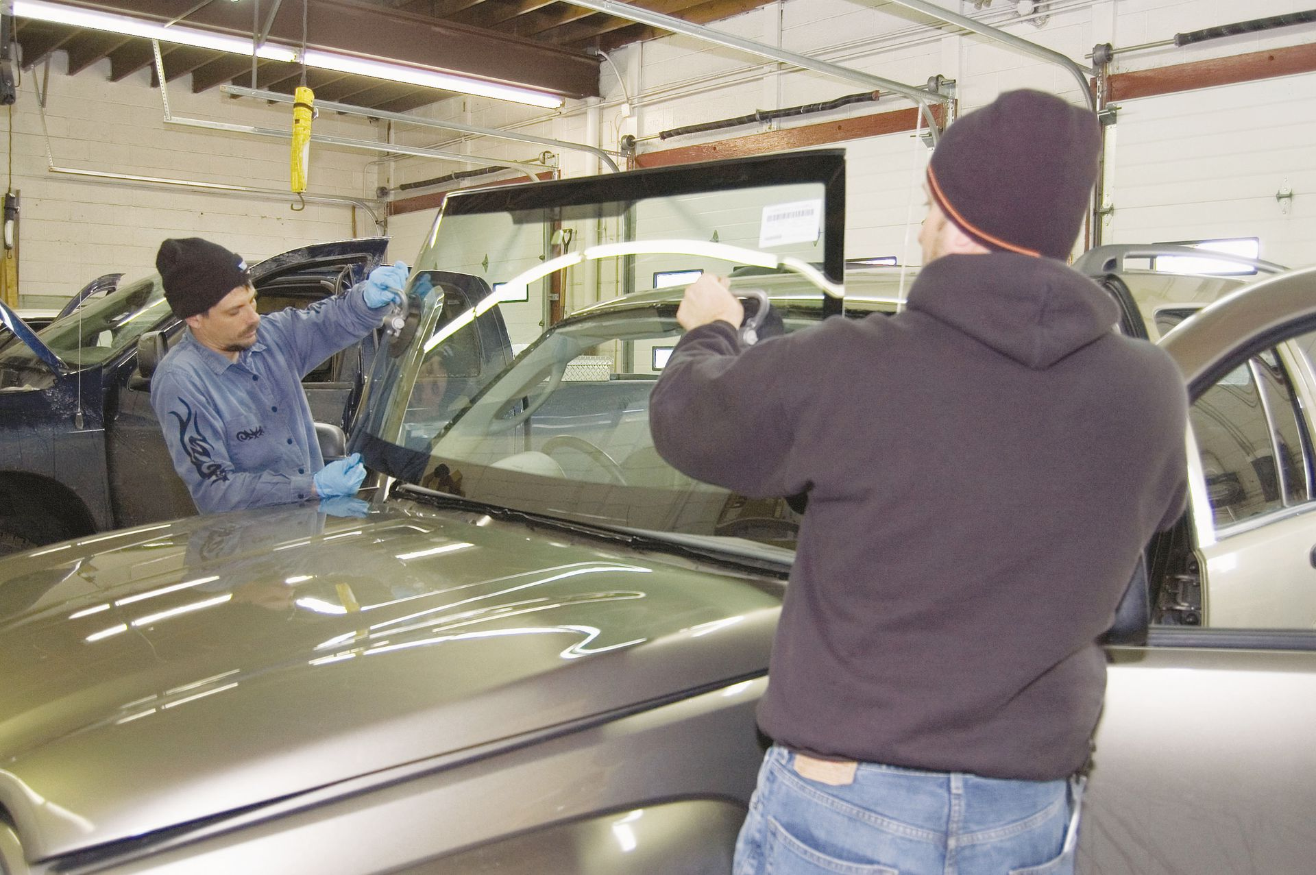 Two workers inspecting a car windshield in an auto repair shop