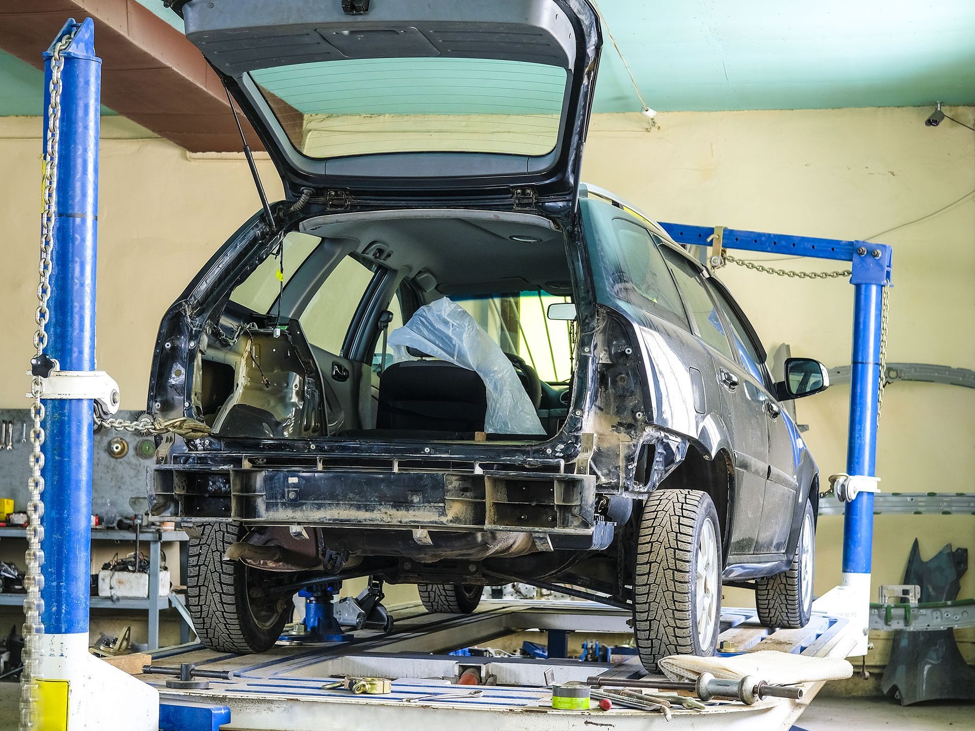 Black SUV on a lift in an auto repair shop, rear hatch open and body partially stripped.