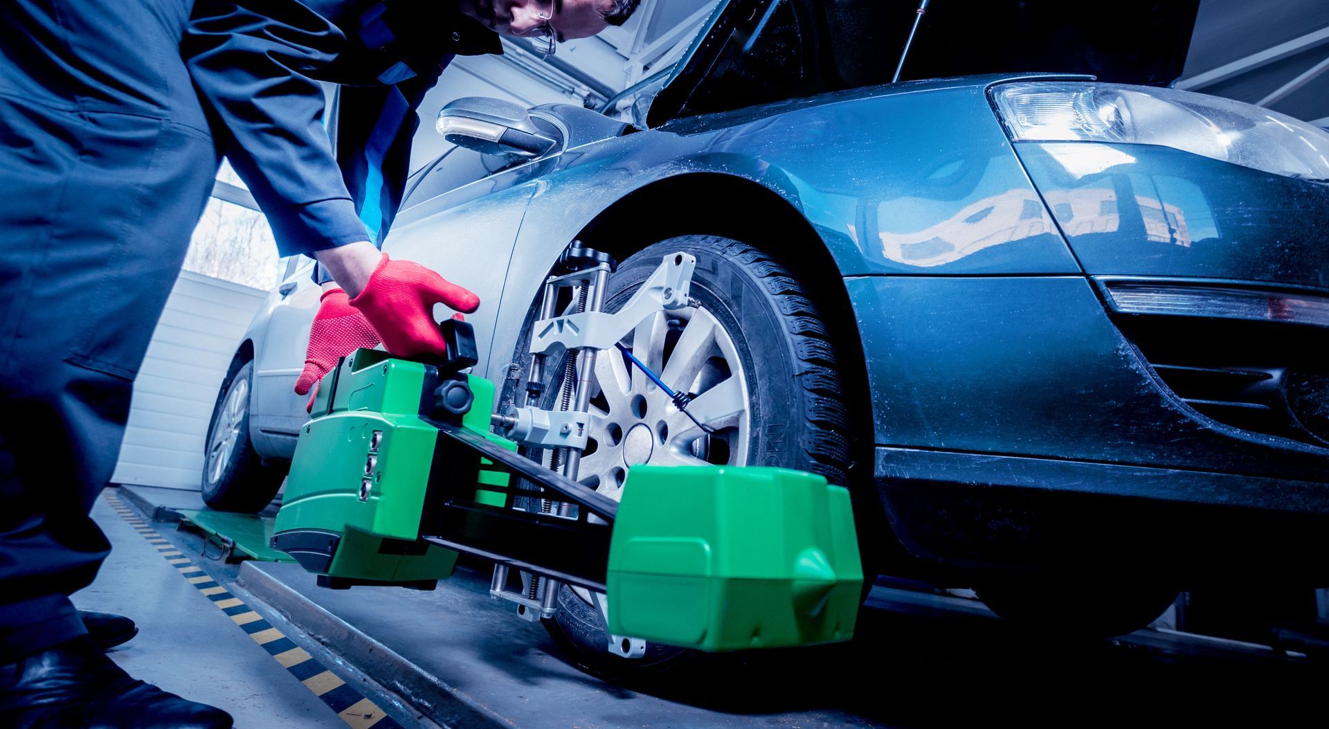 Mechanic using green wheel alignment tool on a blue car in a workshop