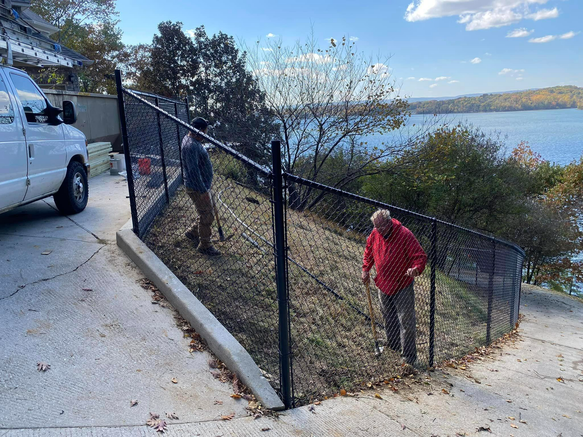 Two men are working on a chain link fence next to a lake.