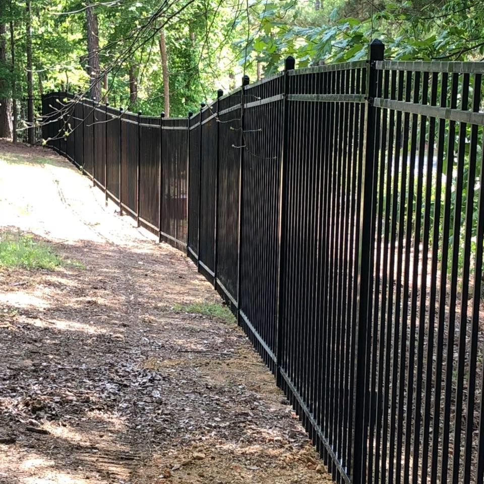 A black metal fence surrounds a dirt path in the woods.