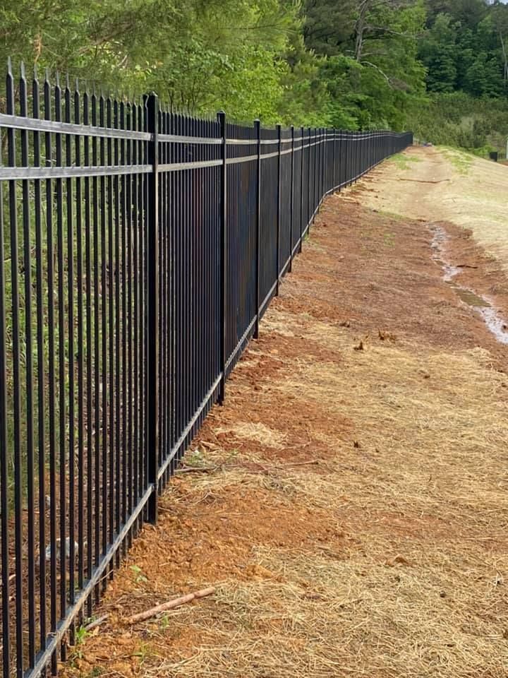 A black metal fence surrounds a dirt field.