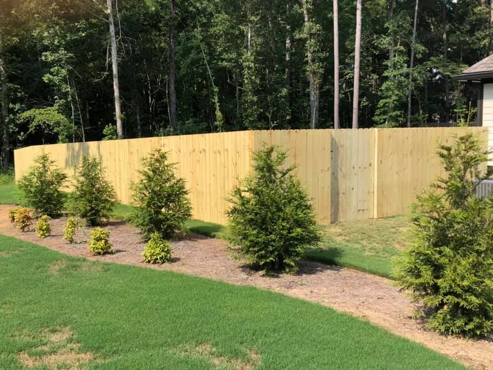 A wooden fence is surrounded by trees and bushes in a yard.