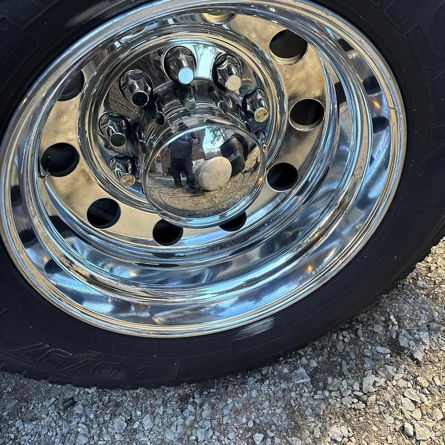 Close-up of a shiny chrome wheel rim with black tire on gravel.