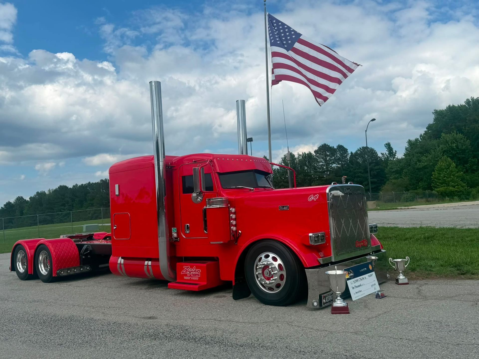 Bright red semi truck parked roadside with an American flag flying above it.