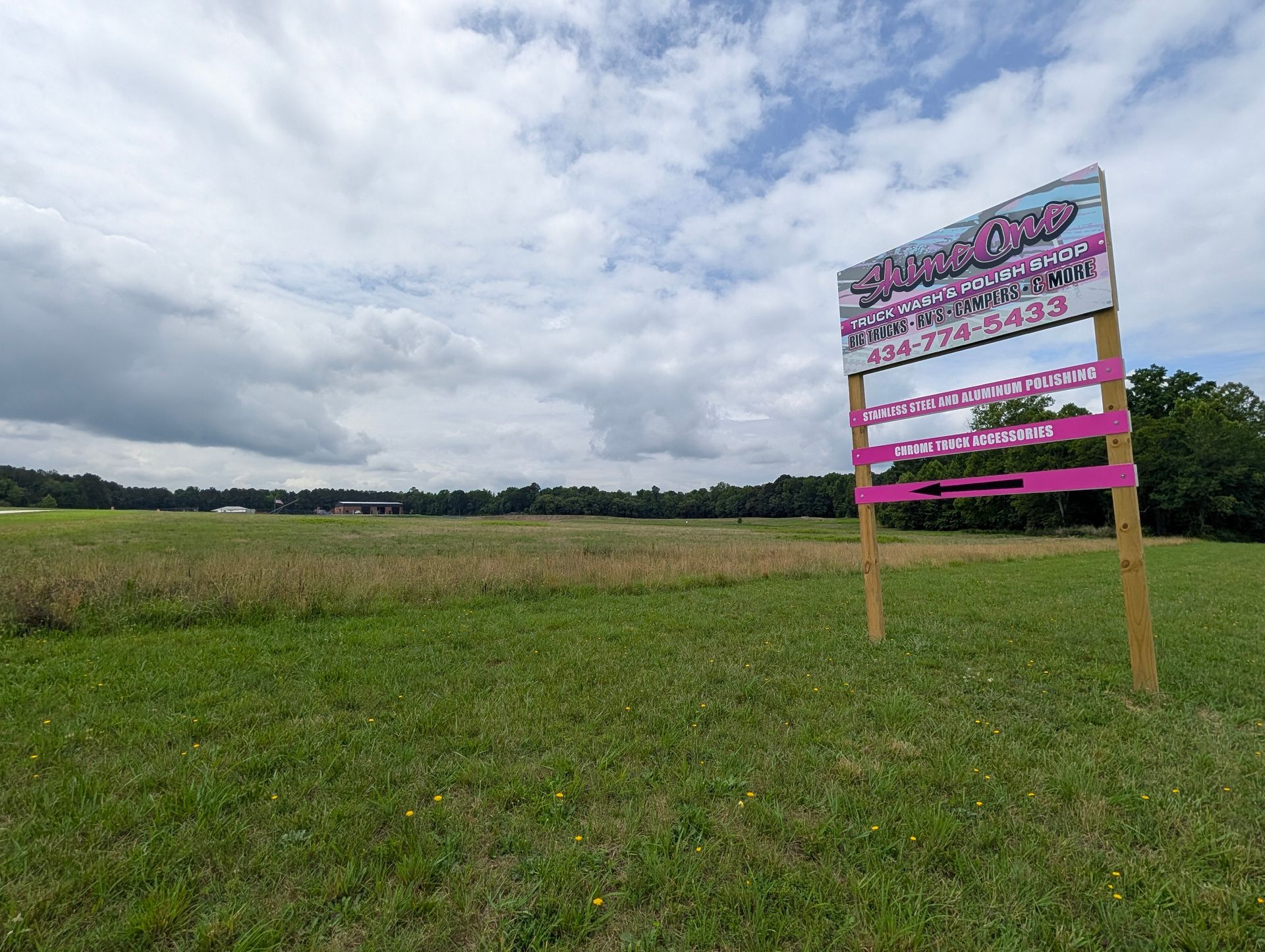 Pink real estate sign in a grassy field under a cloudy sky