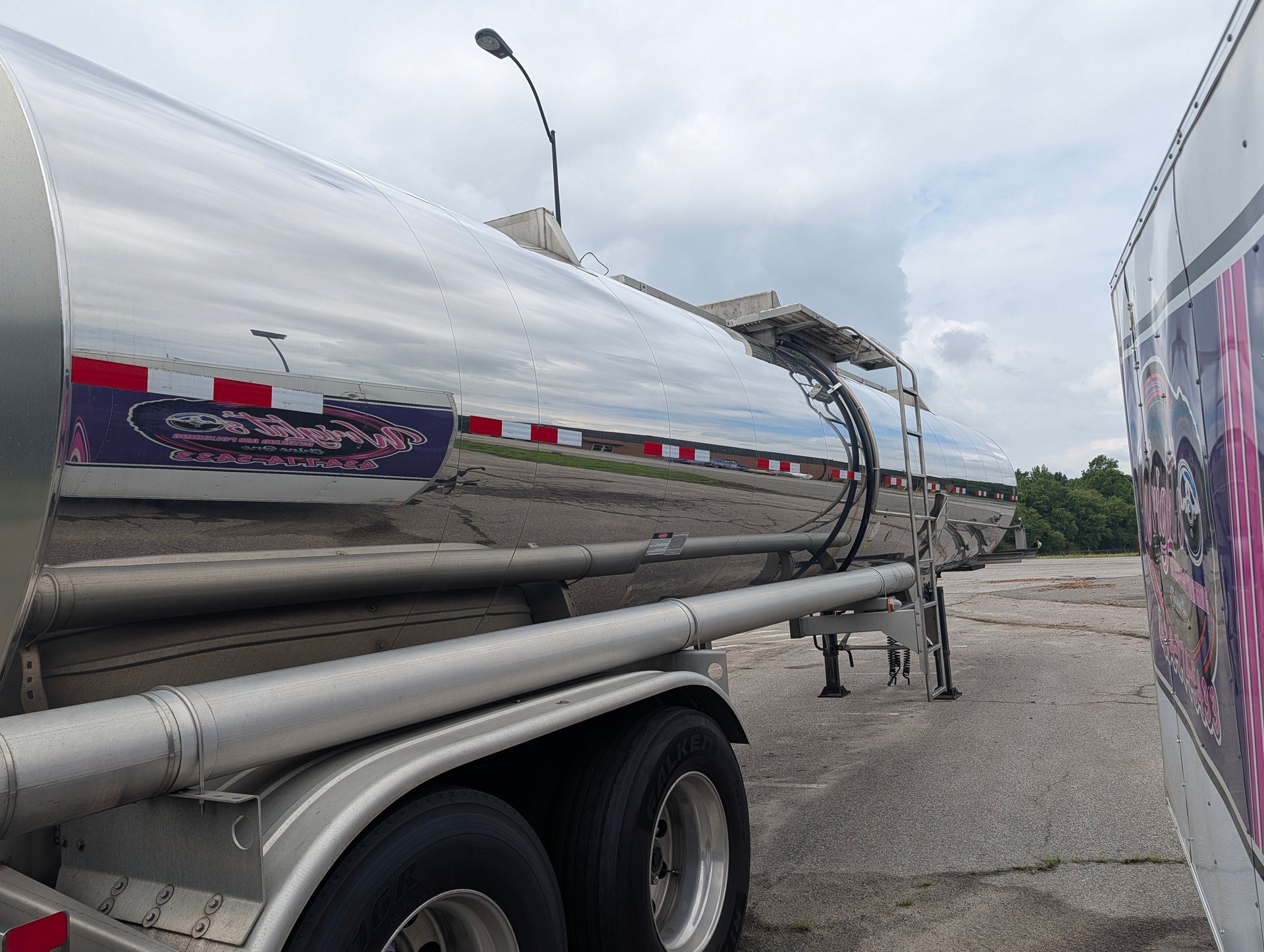 Silver tanker trailer parked on gravel, with cracked top seam and cloudy sky overhead.
