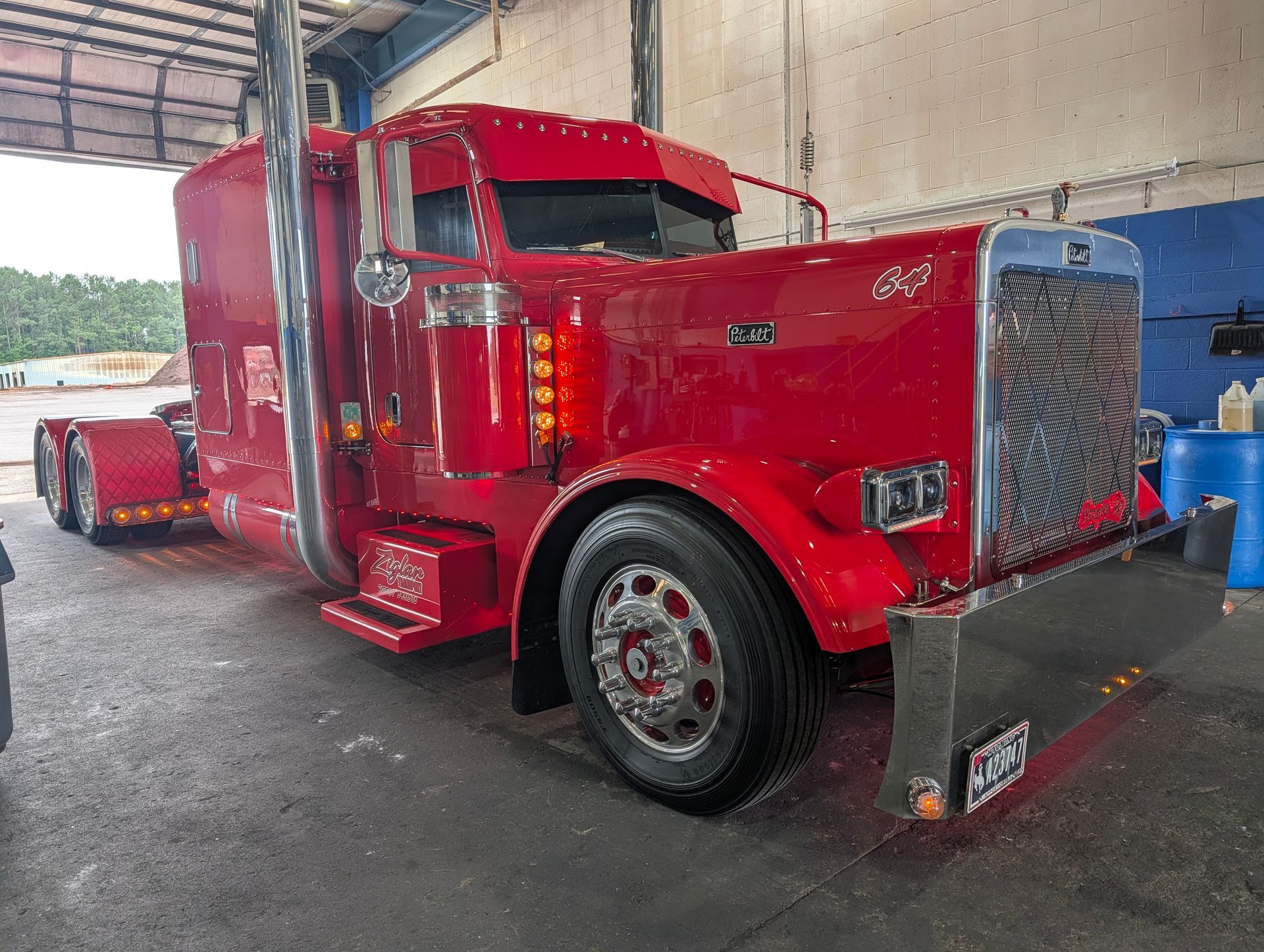 Red semi truck in a garage, with chrome grille and wet floor.