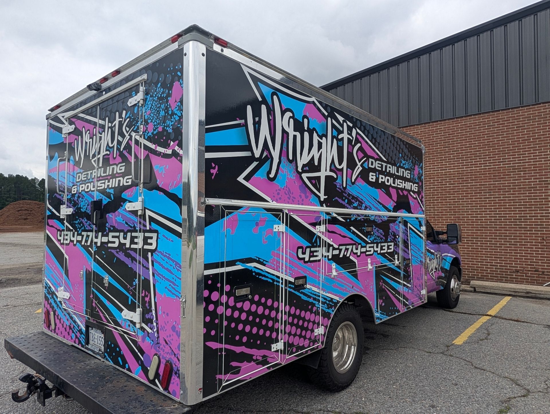 Pink, blue, and black custom trailer with graffiti-style graphics parked beside a brick building.