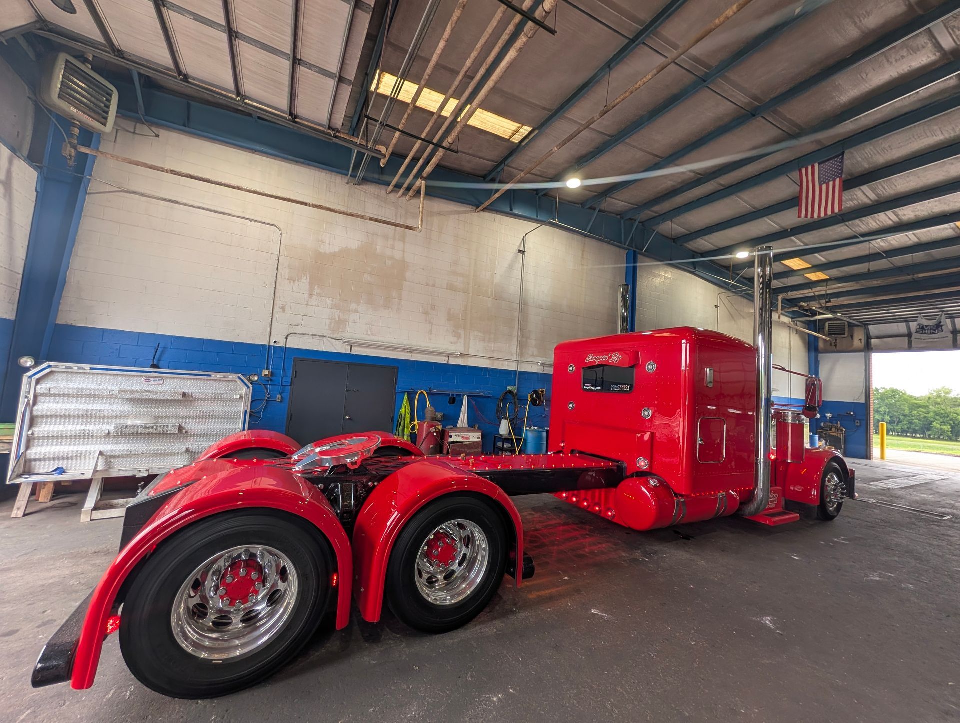 Red semi-truck parked inside a warehouse, with a polished chrome front and twin rear axles.