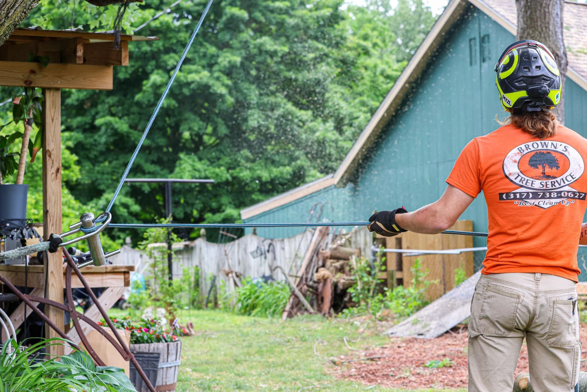 A man in an orange shirt is standing in a yard holding a hose.