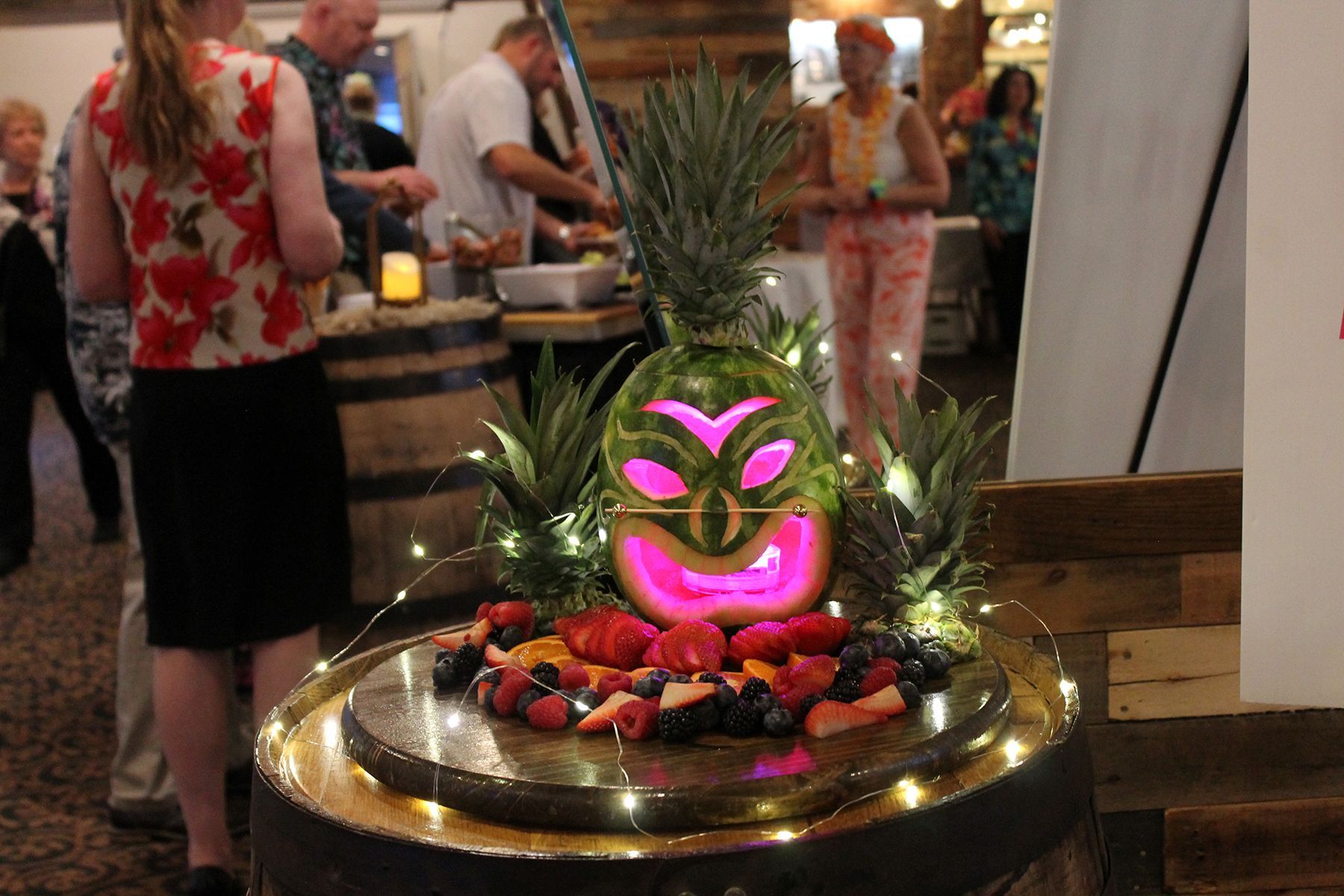 Neon pink pineapple centerpiece on a fruit tray at a cocktail party, with people chatting in the background